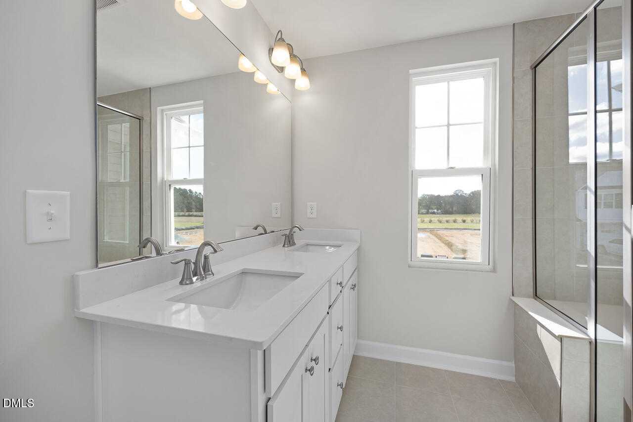 Modern master bathroom with double vanity, glass shower enclosure, and window view in Davidson Homes The Warren, Fuquay-Varina, NC