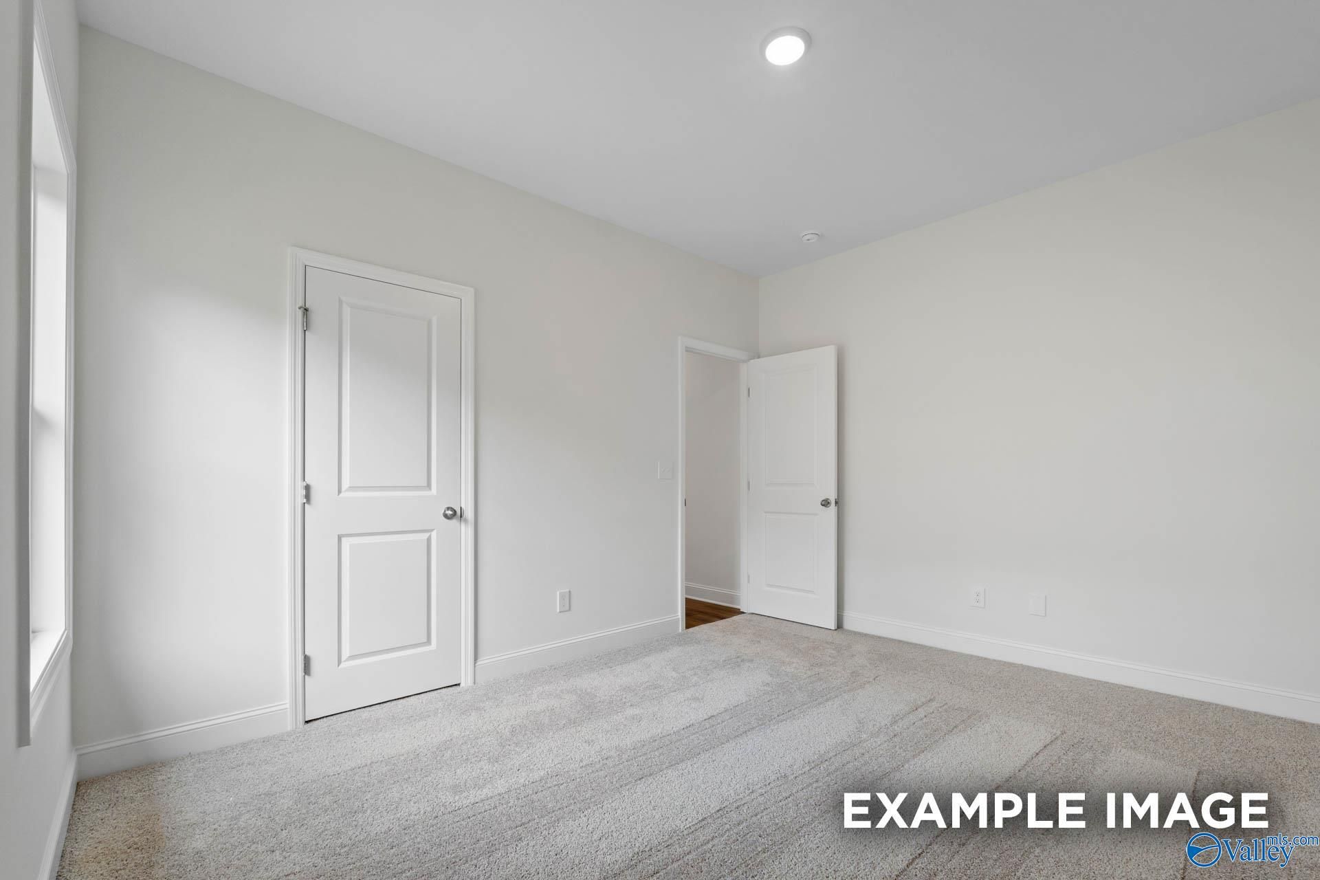 Bright secondary bedroom with neutral walls, beige carpet, and adjacent bath door in Evermore Homes The Daphne E, Harvest AL