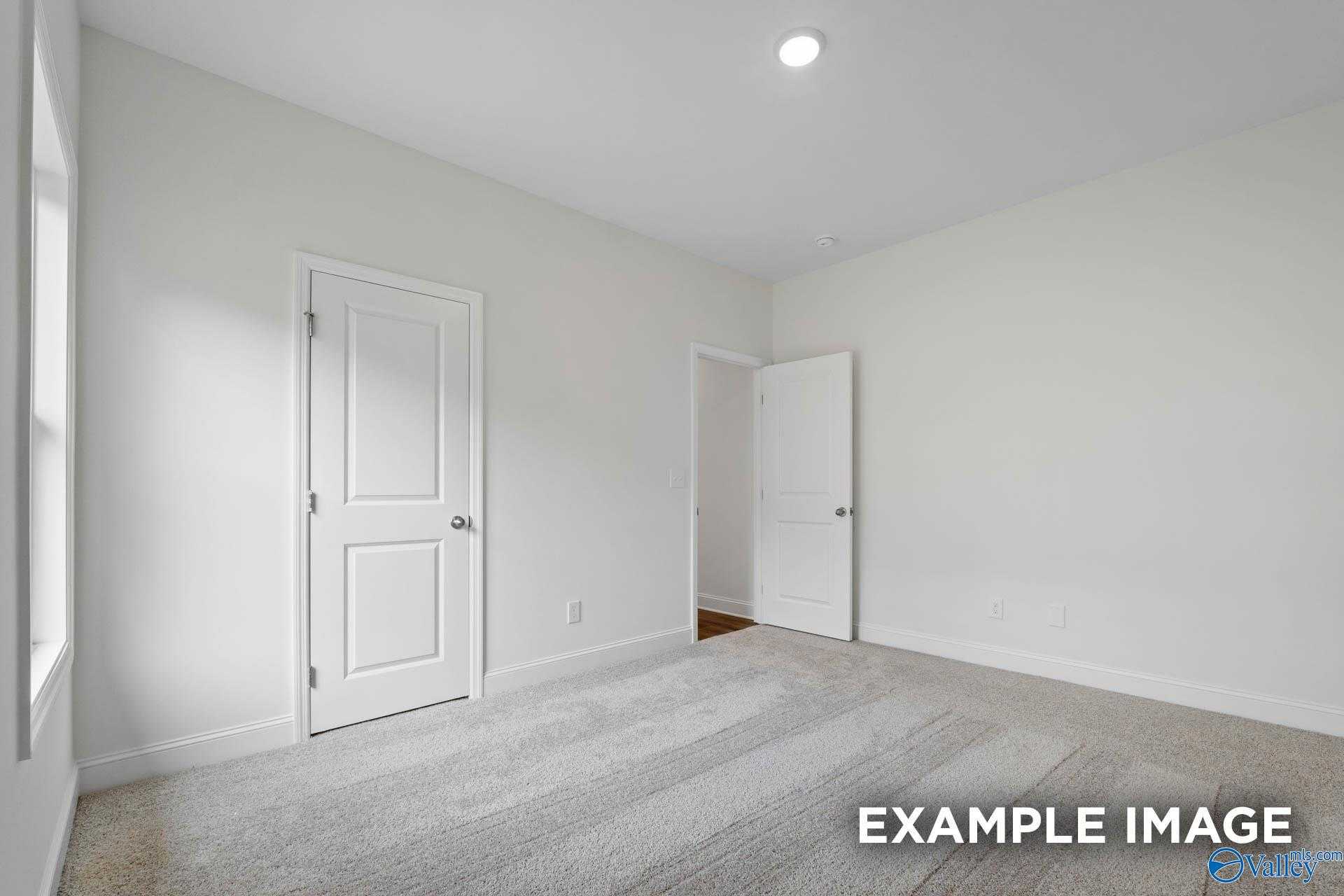 Spacious empty bedroom with neutral walls, white doors, beige carpet, and window in Davidson Homes The Daphne D, Athens, Alabama