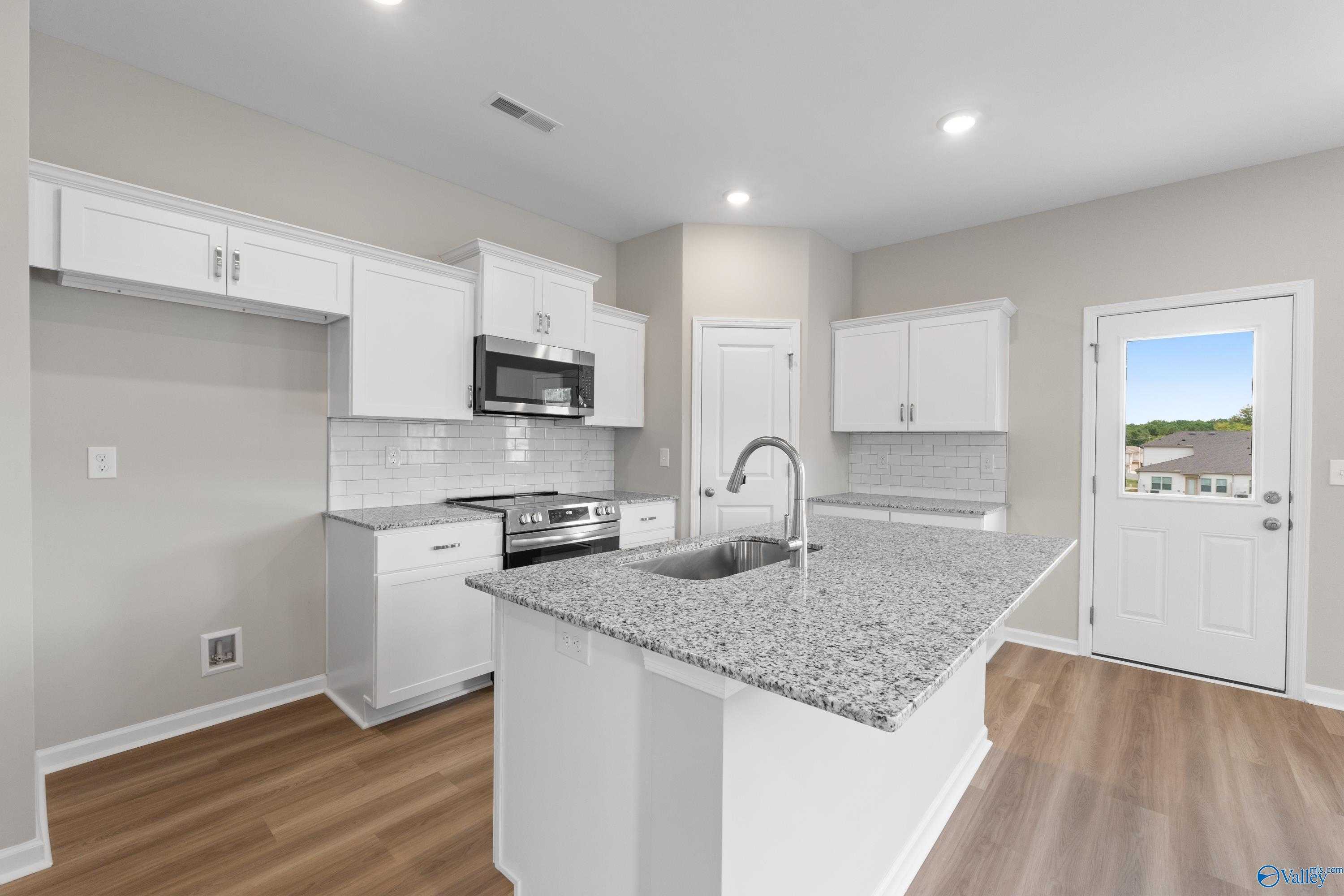 Modern kitchen with white cabinets, granite island, stainless appliances, subway tile backsplash in The Augusta home, Madison Alabama