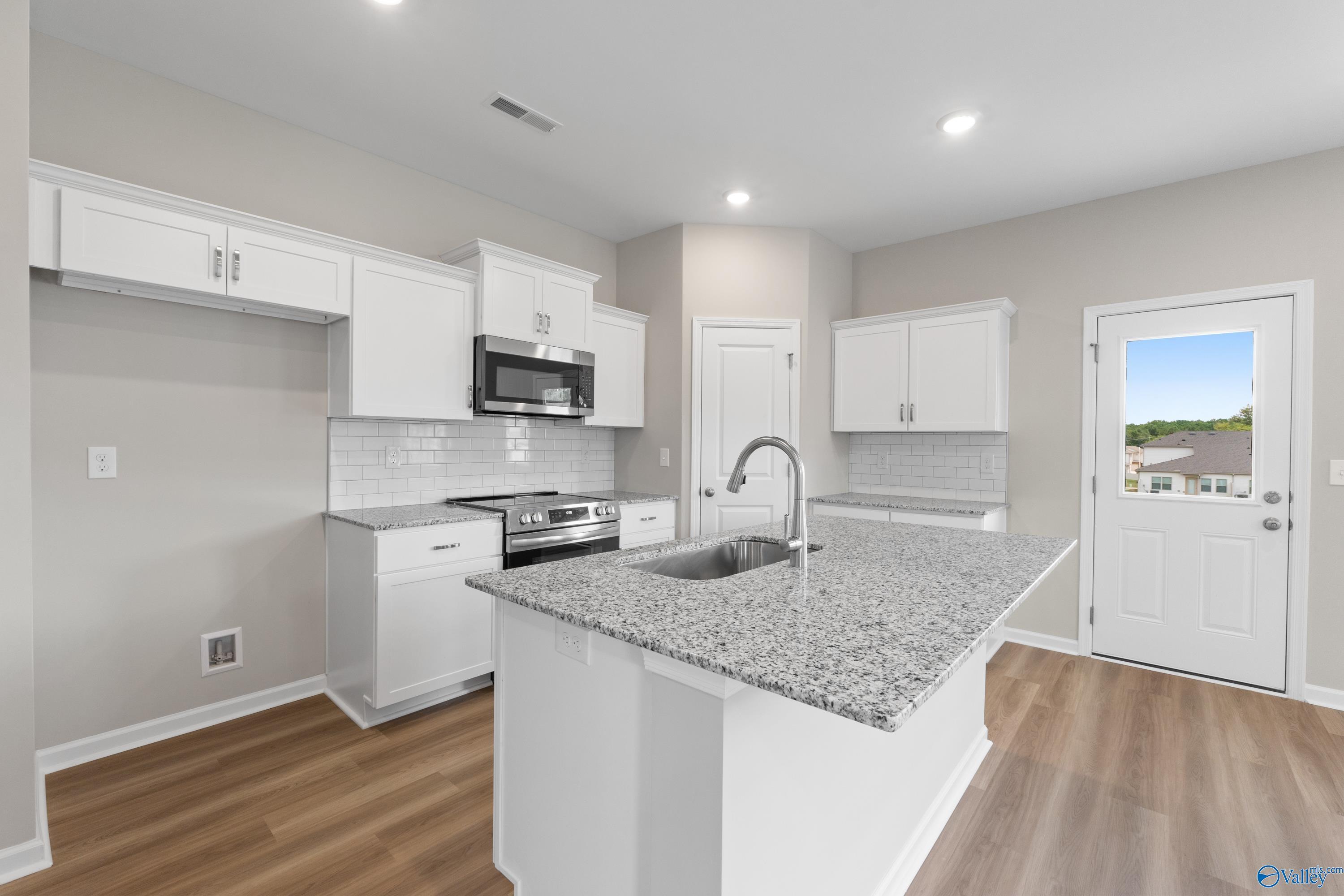Modern kitchen featuring white shaker cabinets, granite island with sink, stainless appliances, subway tile backsplash in Davidson Homes The Augusta, Madison AL