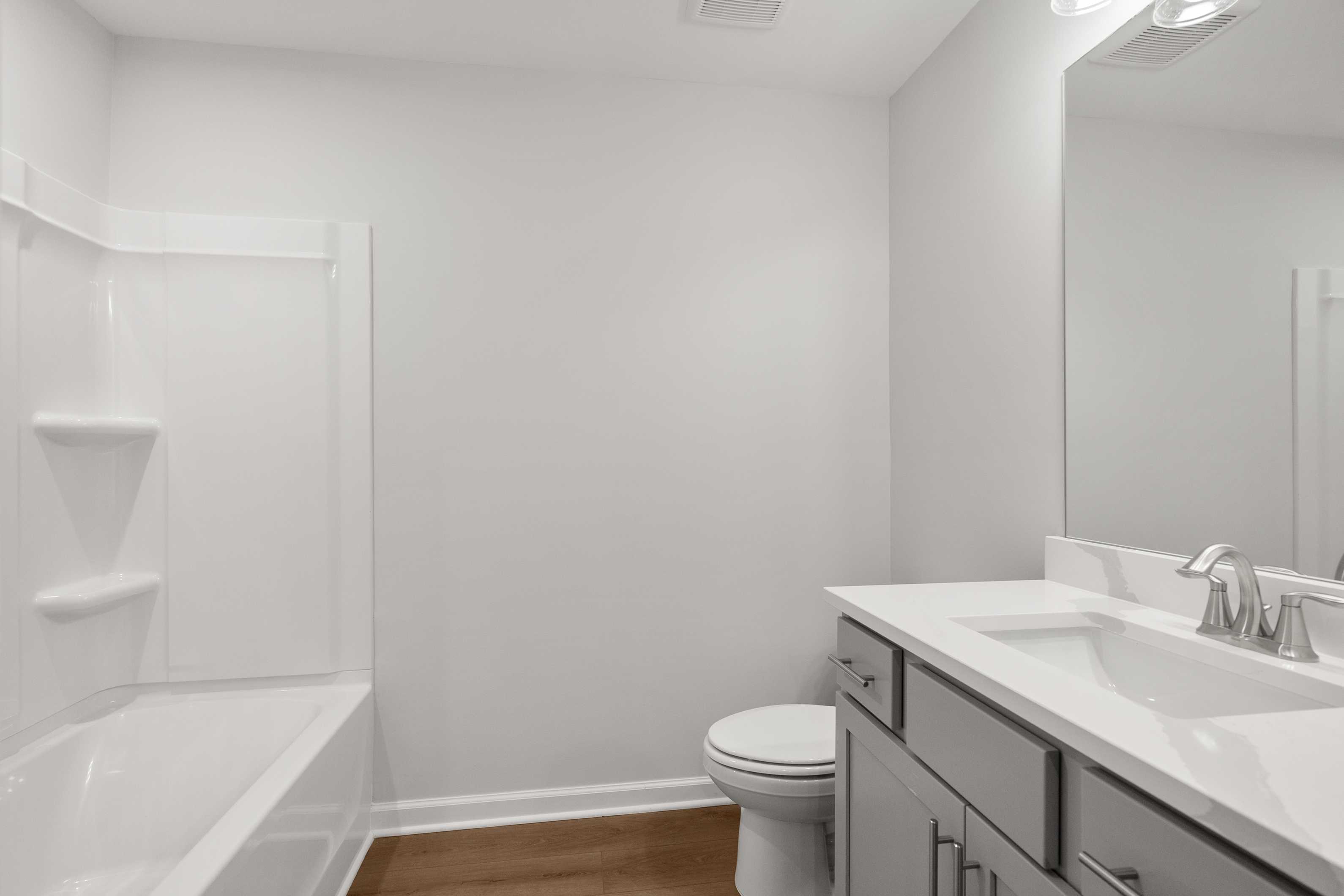 Spacious white bathroom in The Durant A by Davidson Homes with soaking tub, double vanity sink, mirror, and hardwood floors