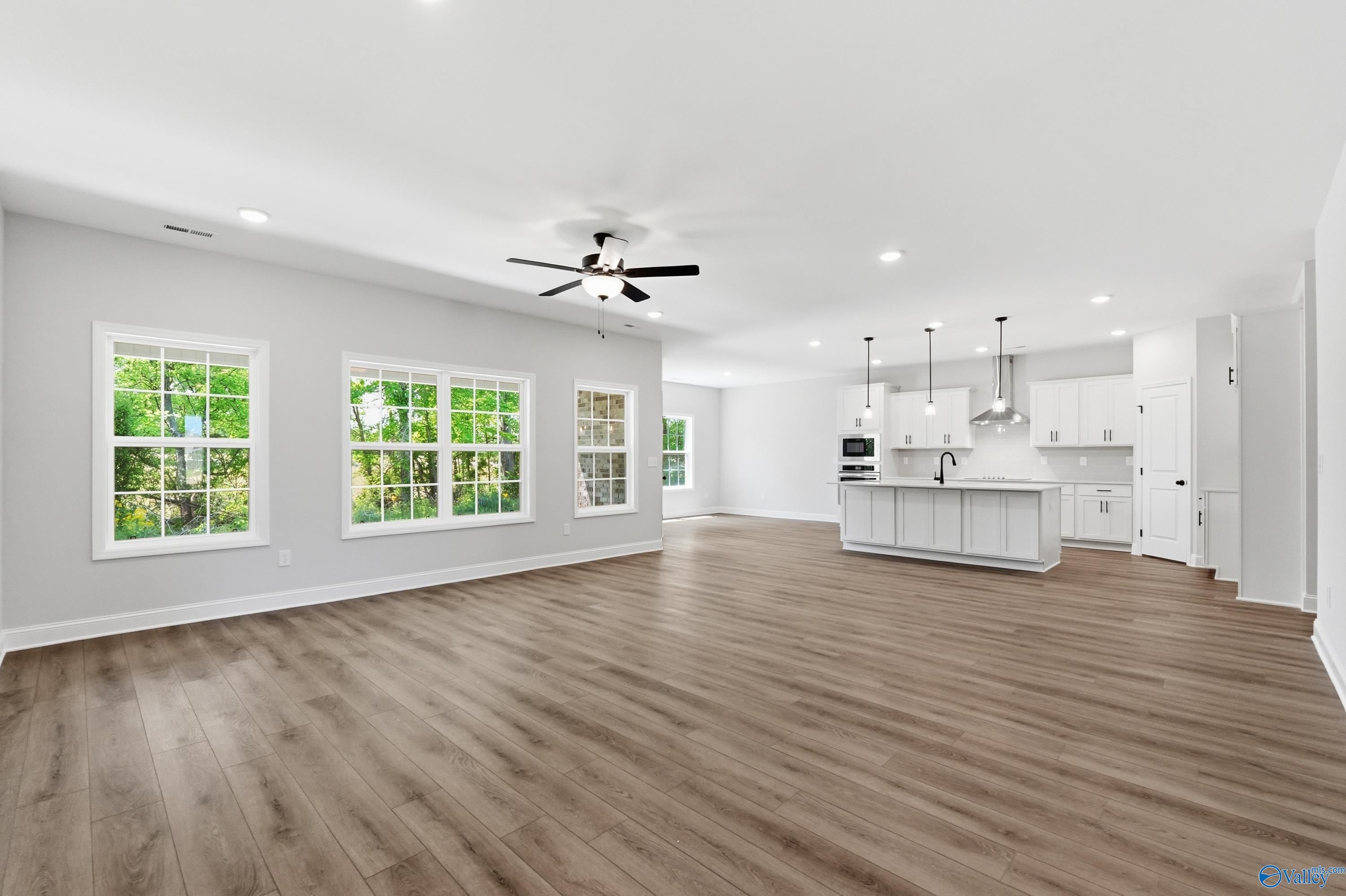 Open-concept kitchen and great room with white shaker cabinets, island sink, pendant lights, and hardwood floors in Davidson Homes The Rockford B, Athens AL