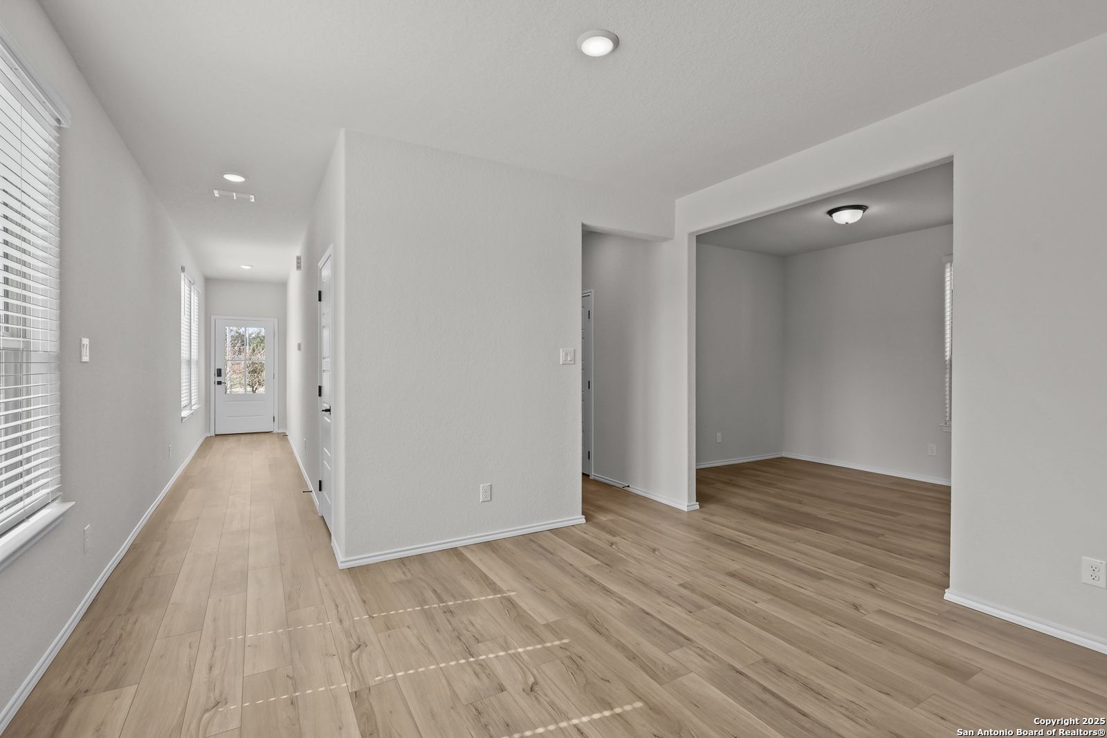 Bright hallway with light hardwood floors, arched entry to empty study, and front door in Davidson Homes The Florence C, San Antonio