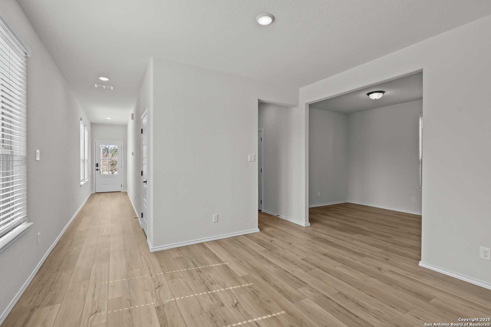Bright hallway with light hardwood floors, arched entry to empty study, and front door in Davidson Homes The Florence C, San Antonio