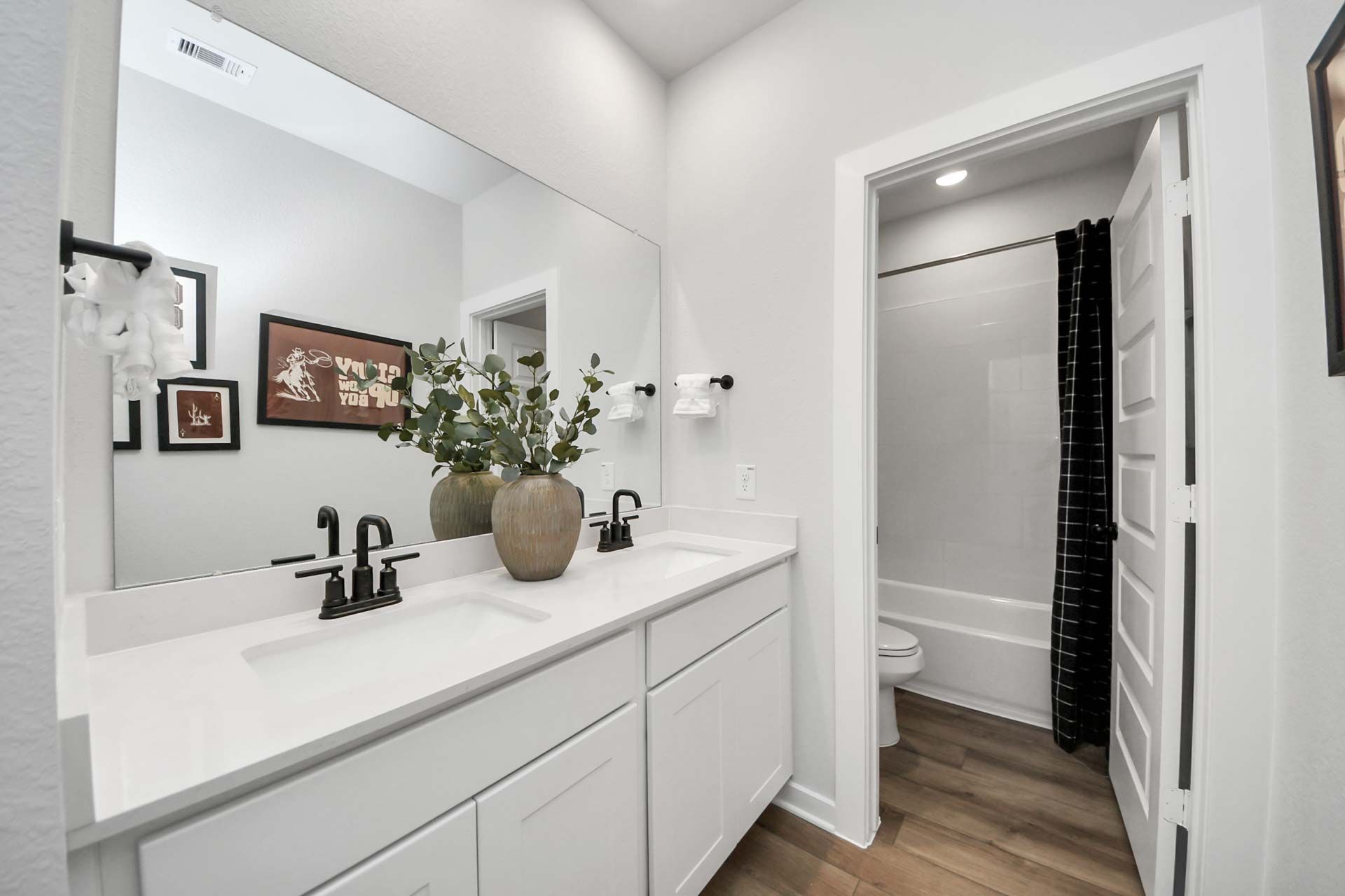 Modern bathroom with white dual vanity, matte black fixtures, and tub-shower combo at Enclave at Newport in Crosby, TX.