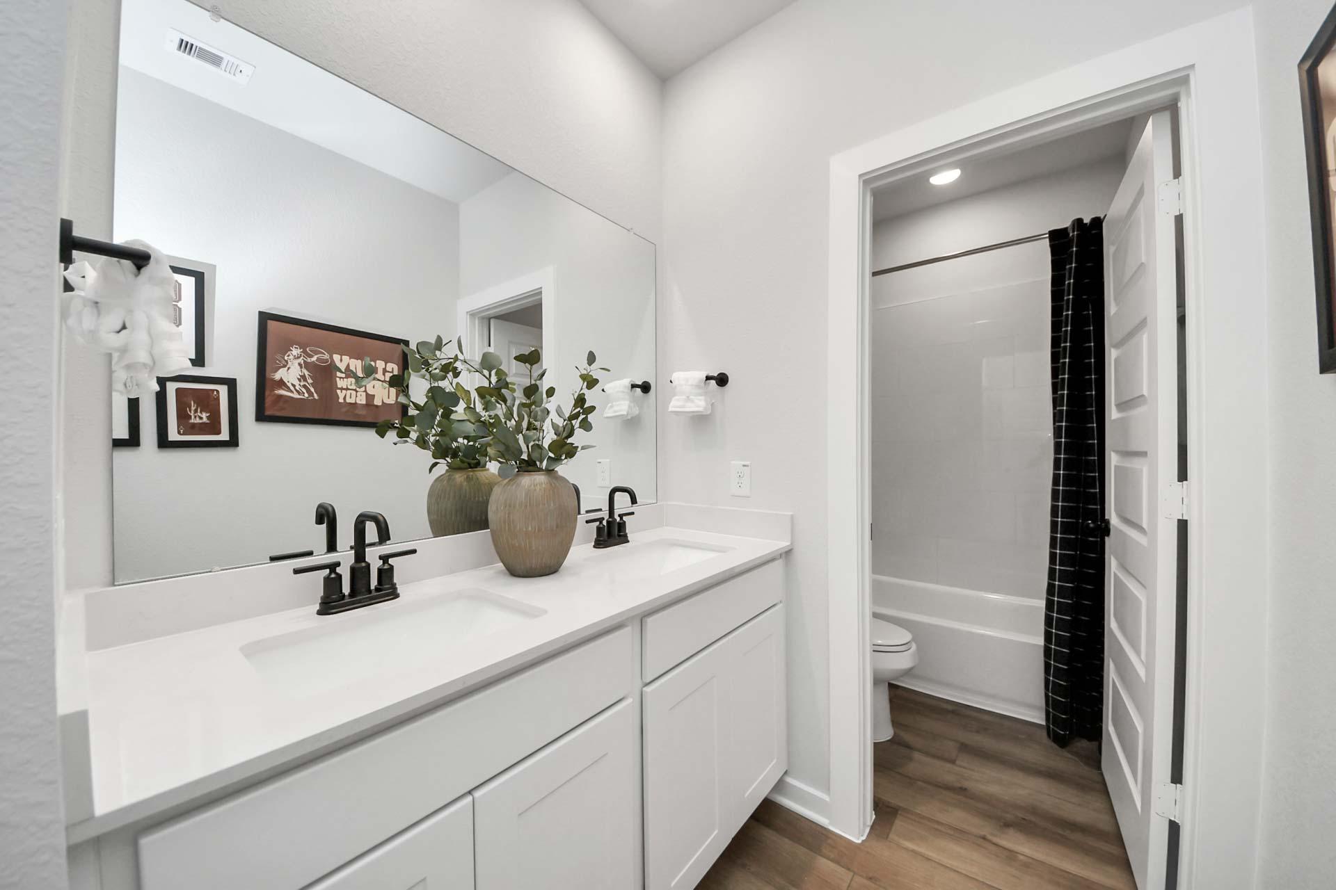 Modern bathroom with white dual vanity, matte black fixtures, and tub-shower combo at Enclave at Newport in Crosby, TX.