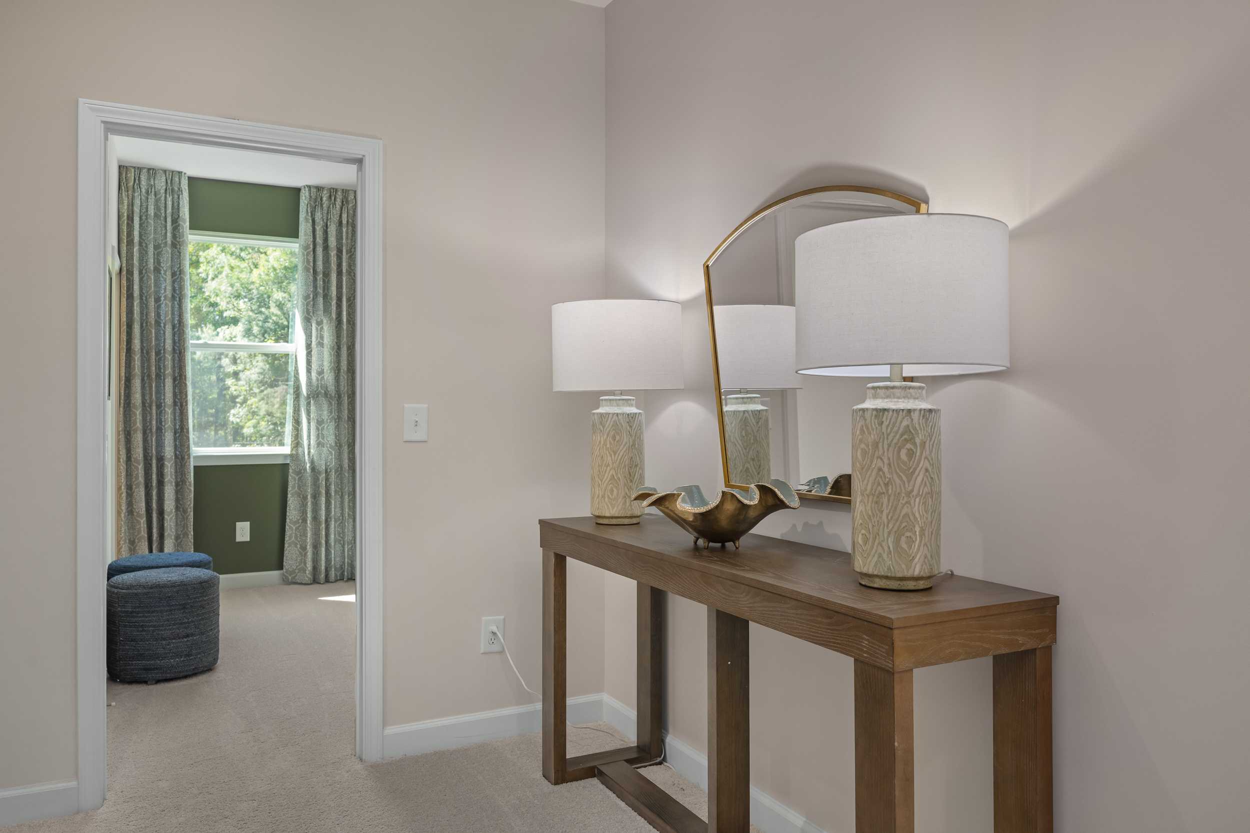 Elegant upper-floor hallway in The Hickory II E master suite with wooden console table, gold arched mirror, and lamps