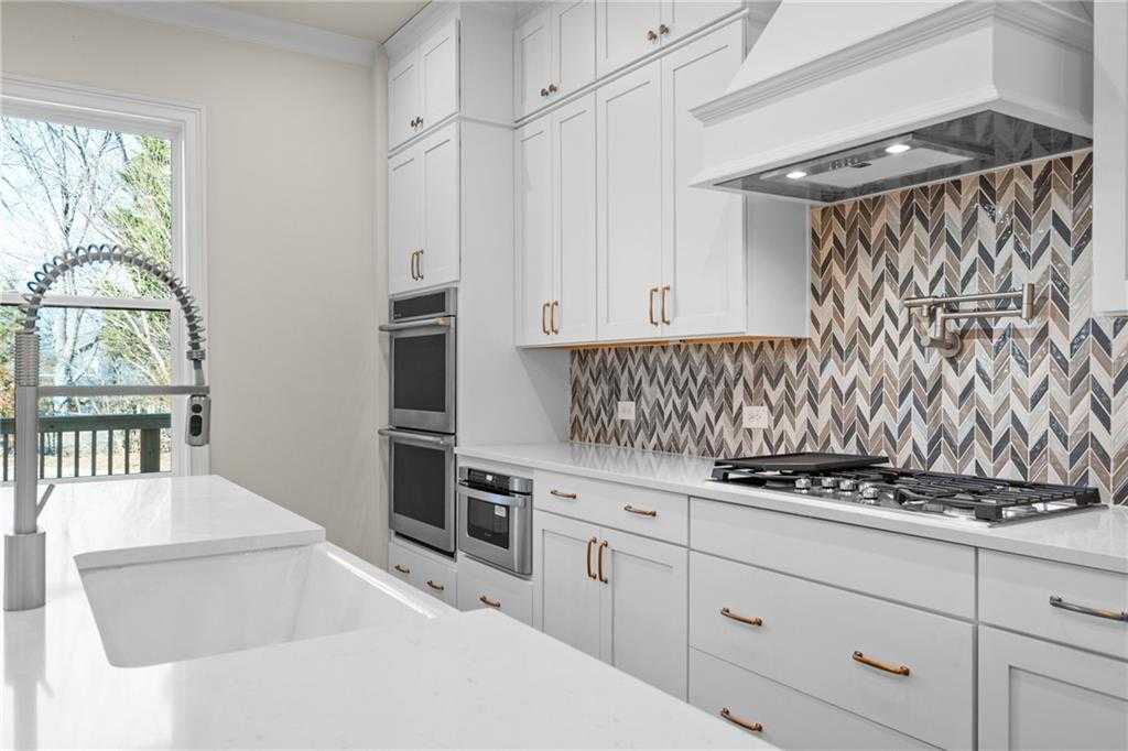 Modern white kitchen with shaker cabinets, quartz island, farmhouse sink, gas range, double ovens, chevron backsplash in Davidson Homes Arlington A, East Cobb