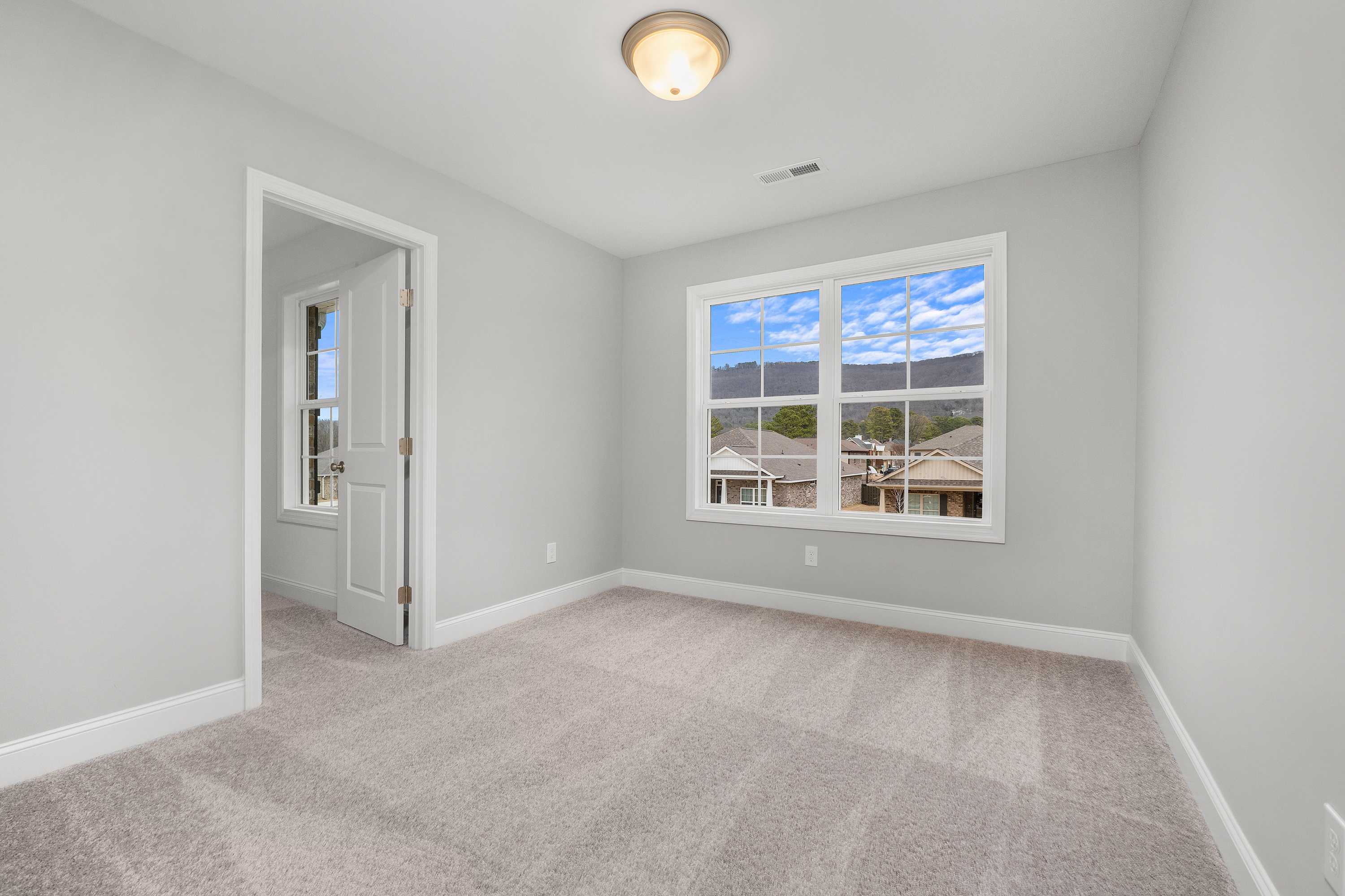 Upper floor bedroom in The Aiken by Davidson Homes, light gray walls, plush carpet, large window with neighborhood view