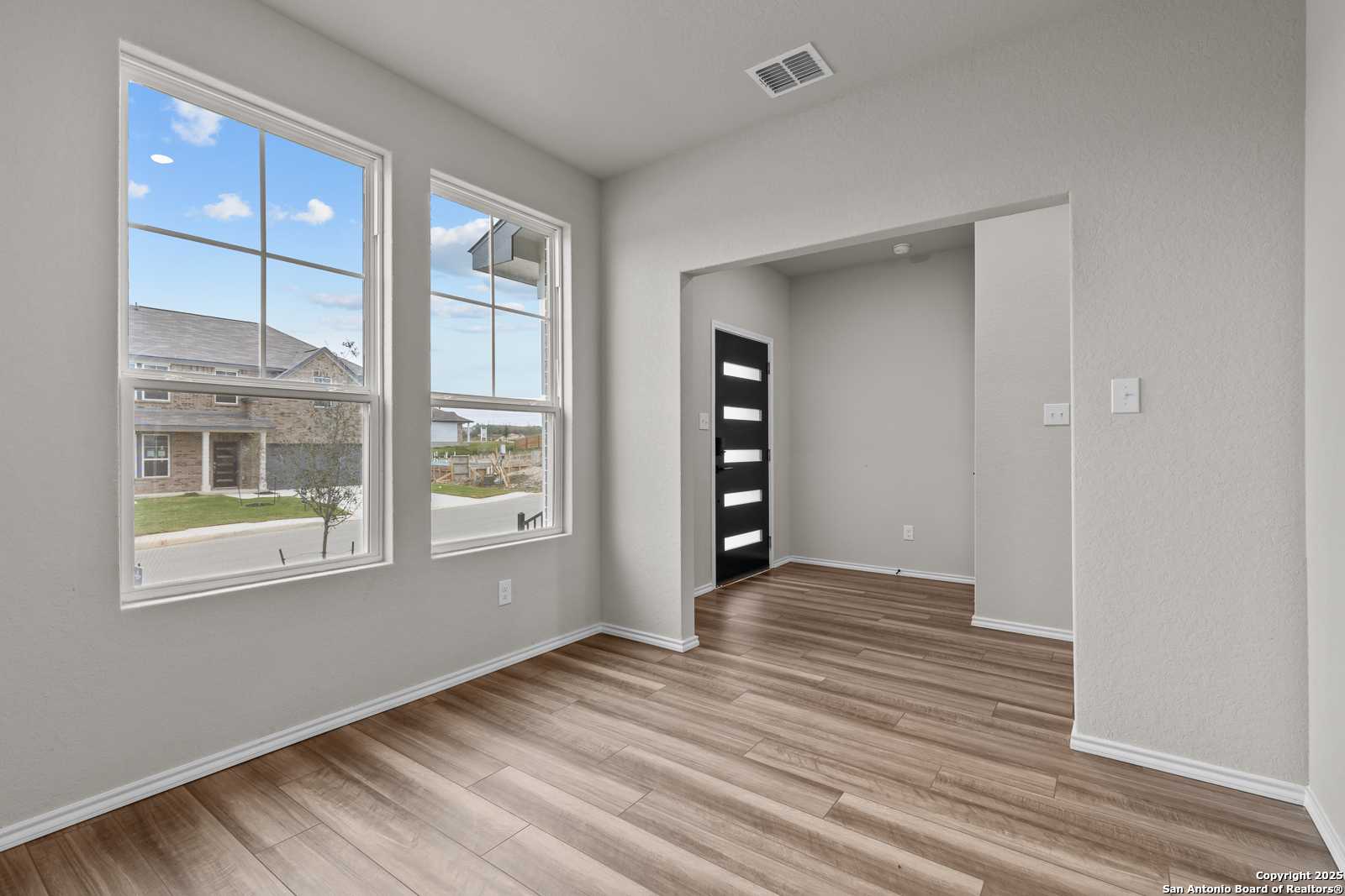 Bright study with large windows overlooking neighborhood, light gray walls, hardwood floors, and modern black door in Davidson Homes The Murray I, San Antonio