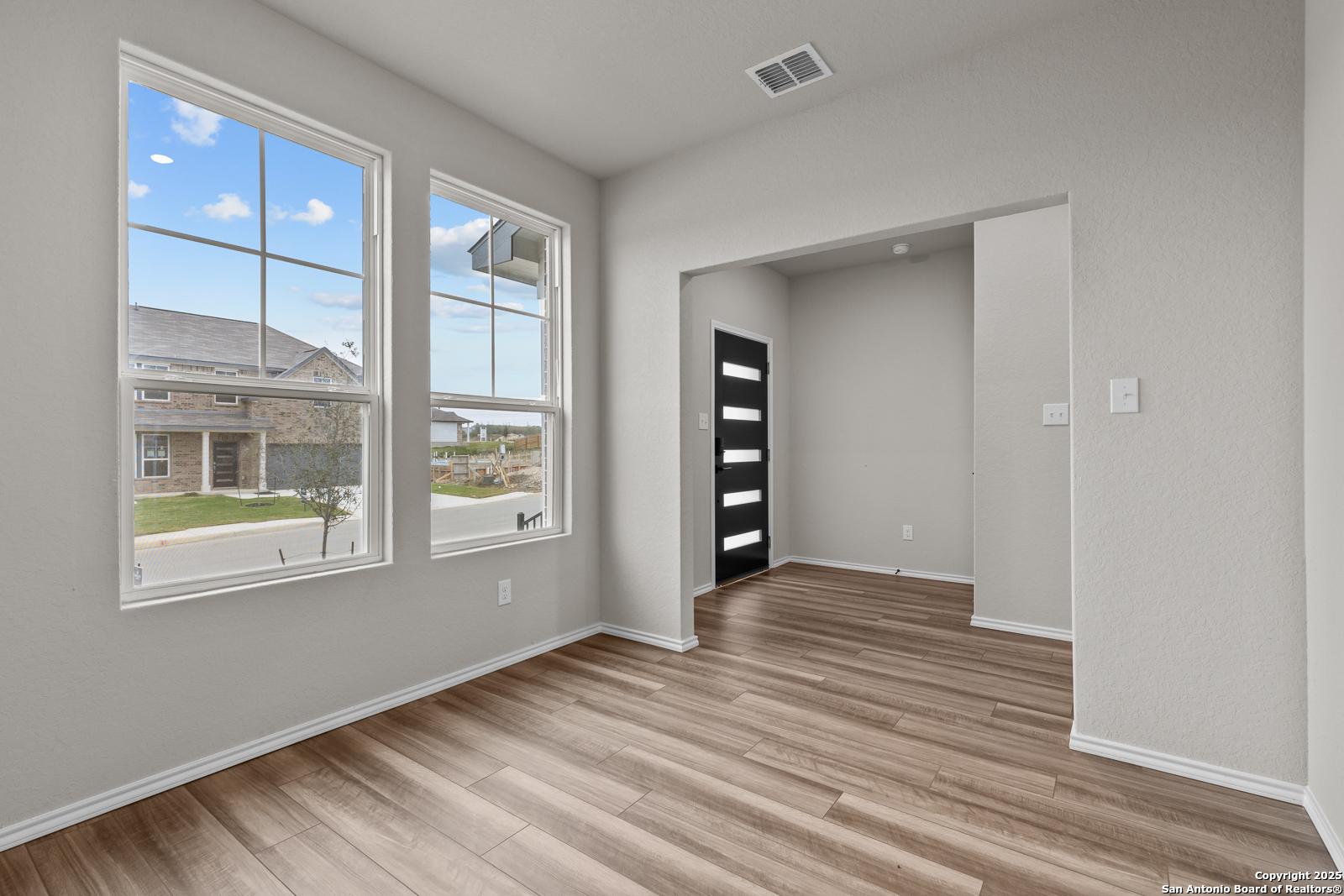 Bright study with large windows overlooking neighborhood, light gray walls, hardwood floors, and modern black door in Davidson Homes The Murray I, San Antonio