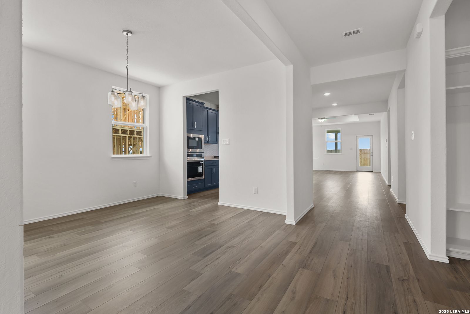 Open dining area with modern chandelier and hardwood floors adjacent to navy blue kitchen in Davidson Homes The Glenwood E, Elmendorf TX
