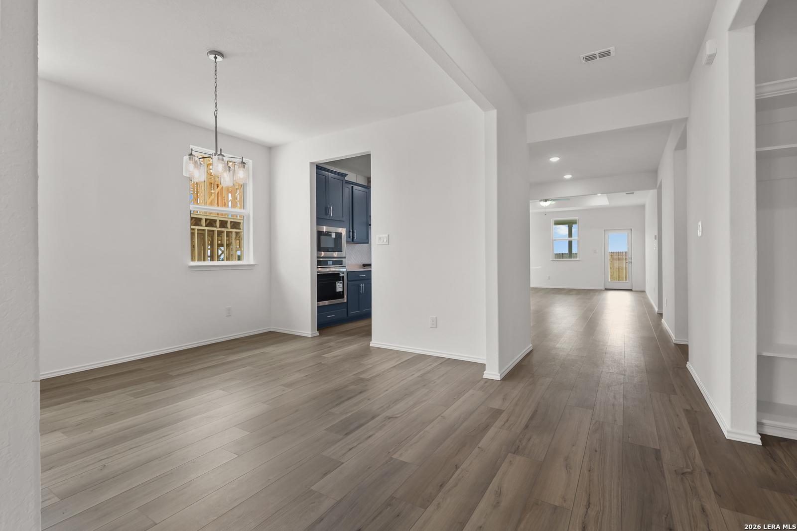 Open dining area with modern chandelier and hardwood floors adjacent to navy blue kitchen in Davidson Homes The Glenwood E, Elmendorf TX
