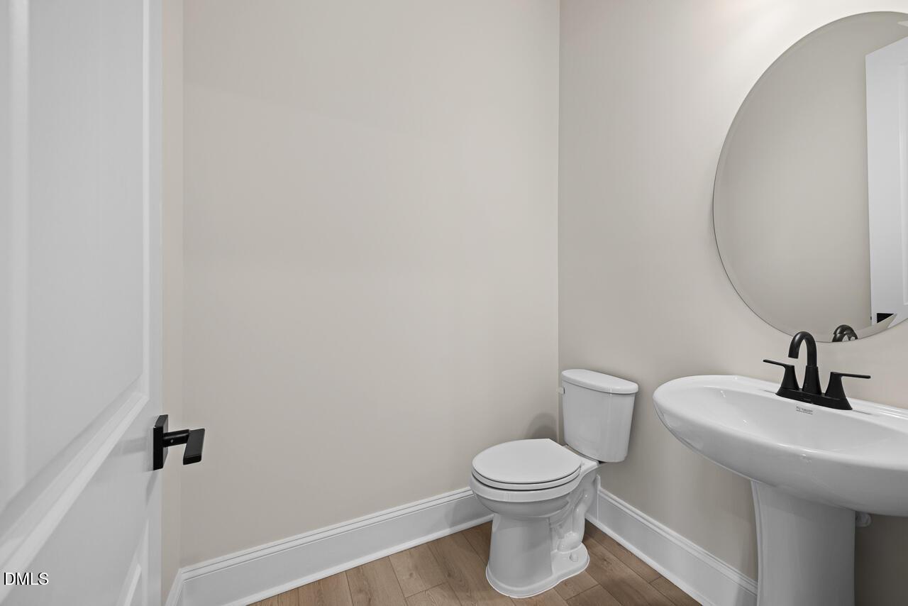 Elegant powder room with pedestal sink, round mirror, and black fixtures in Davidson Homes The Crawford D, Wake Forest, NC