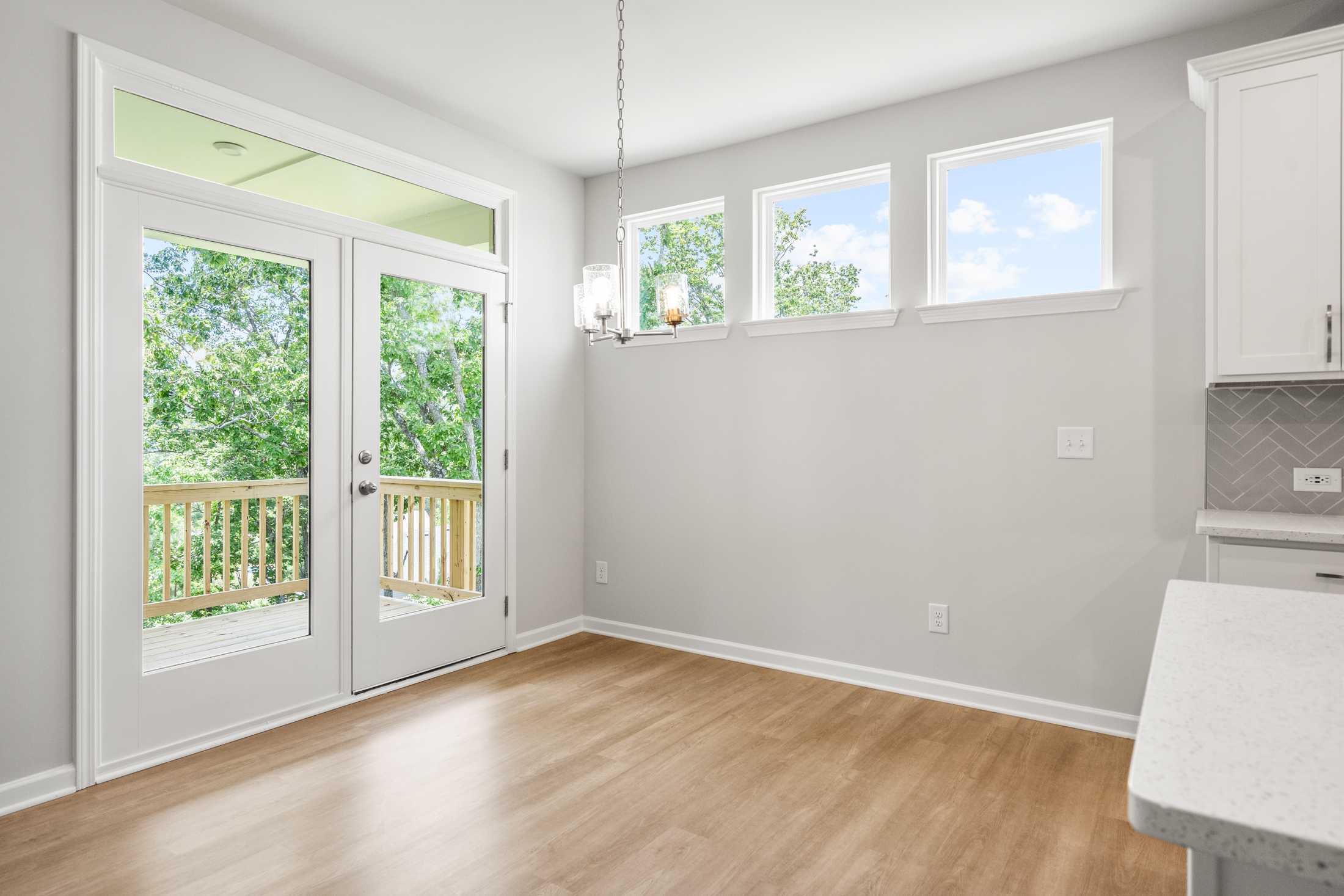 Spacious breakfast nook in The Ash B home with French doors to wooded deck, quartz counters, white cabinets, and abundant natural light