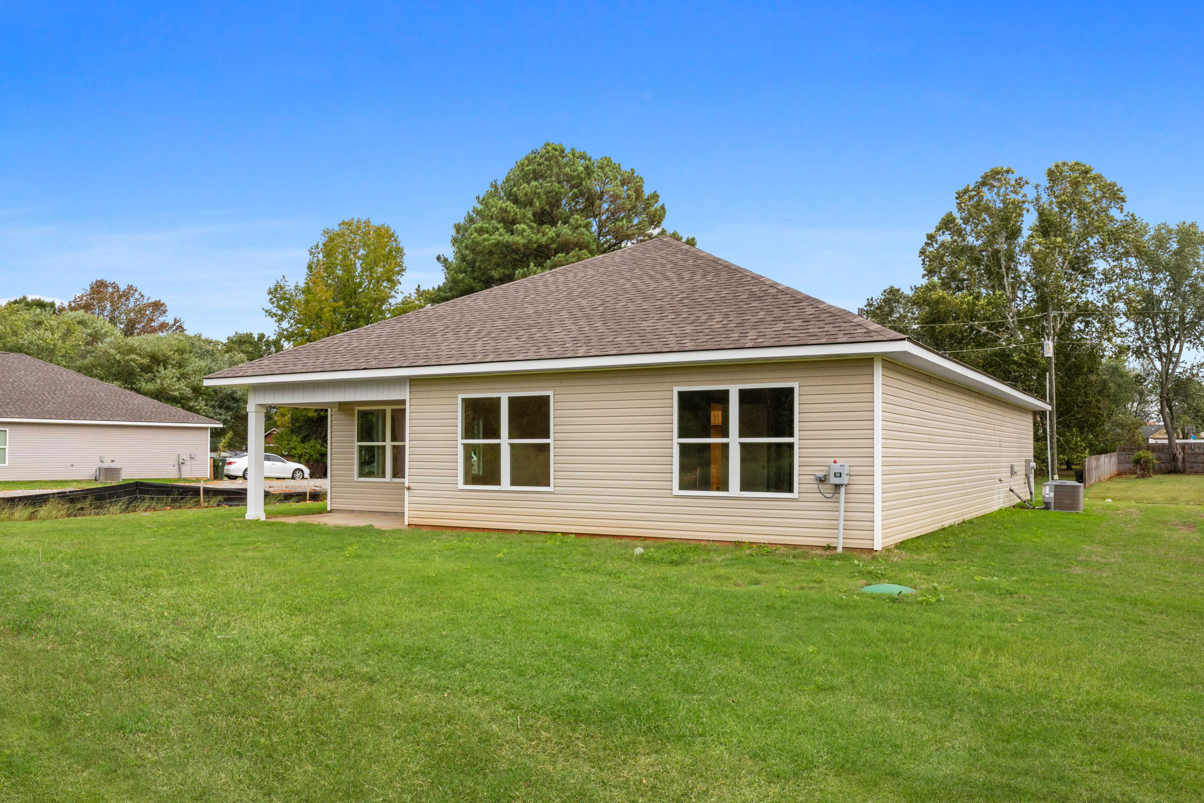 Single-story beige home side exterior at Collins Lane in Meridianville, Alabama with covered patio, large windows, and green lawn