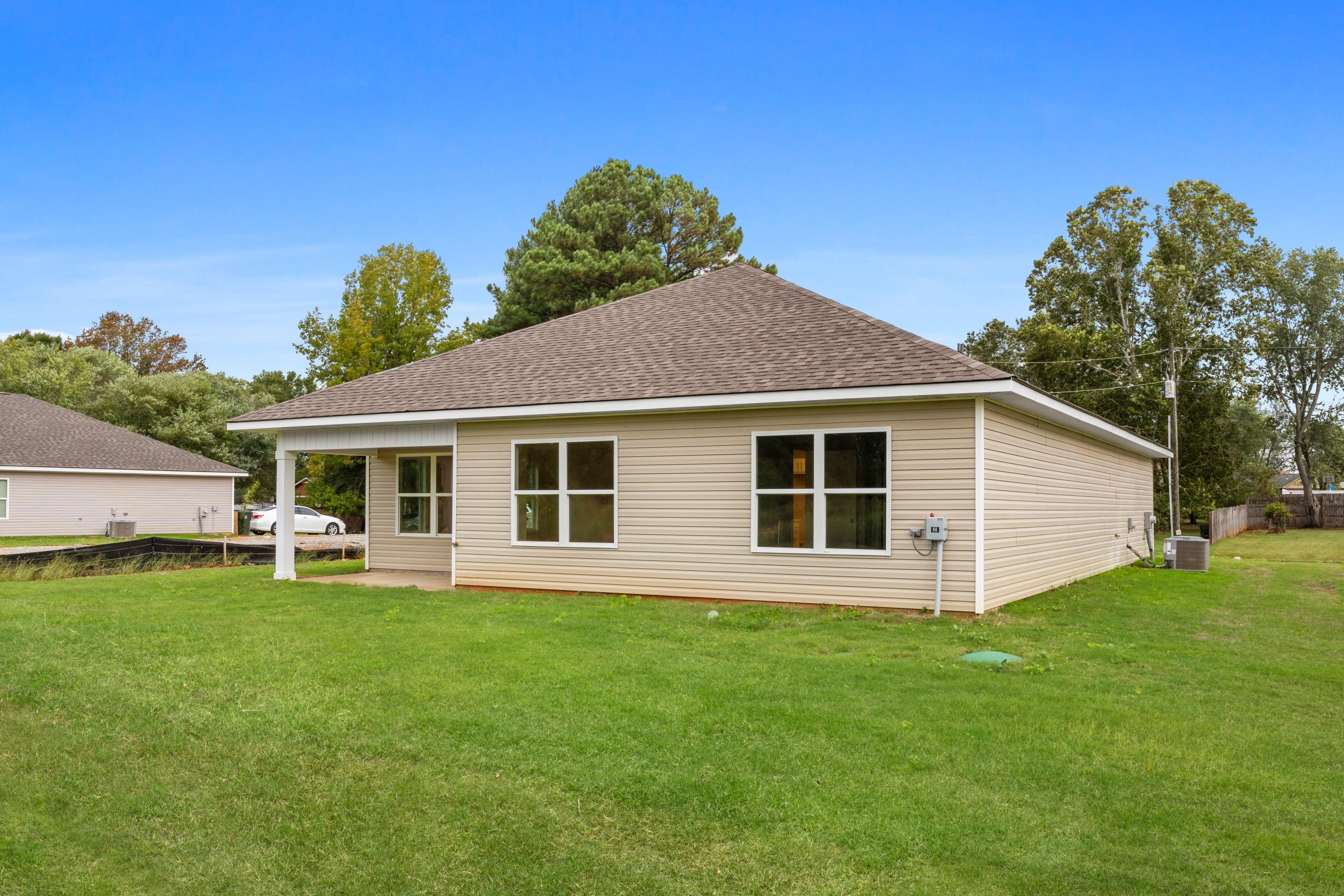 Single-story beige home side exterior at Collins Lane in Meridianville, Alabama with covered patio, large windows, and green lawn