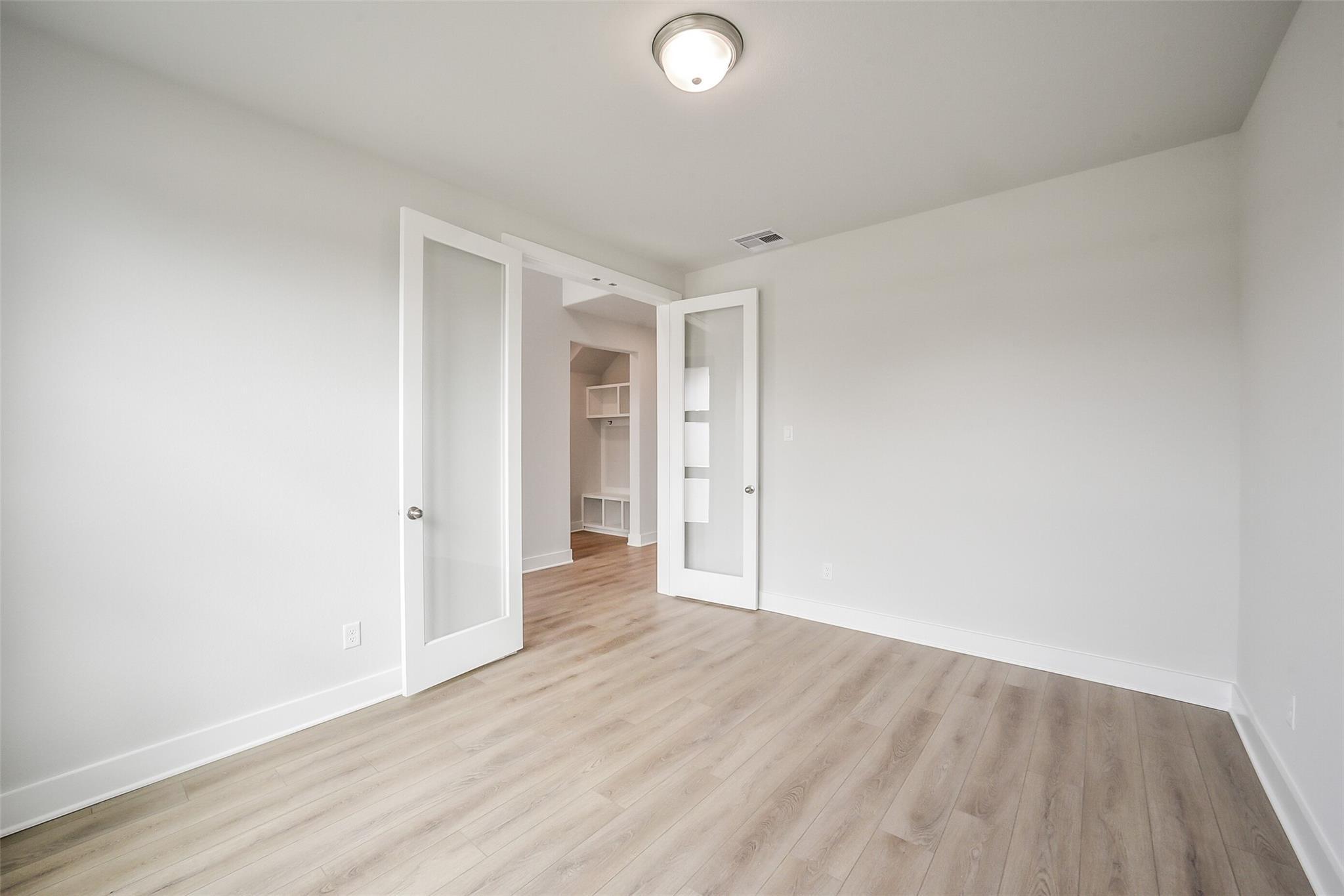 Spacious empty study with white walls, light oak floors, and open glass French doors to built-in shelving in 4-bedroom Davidson Homes The Philip B, Rosharon Texas