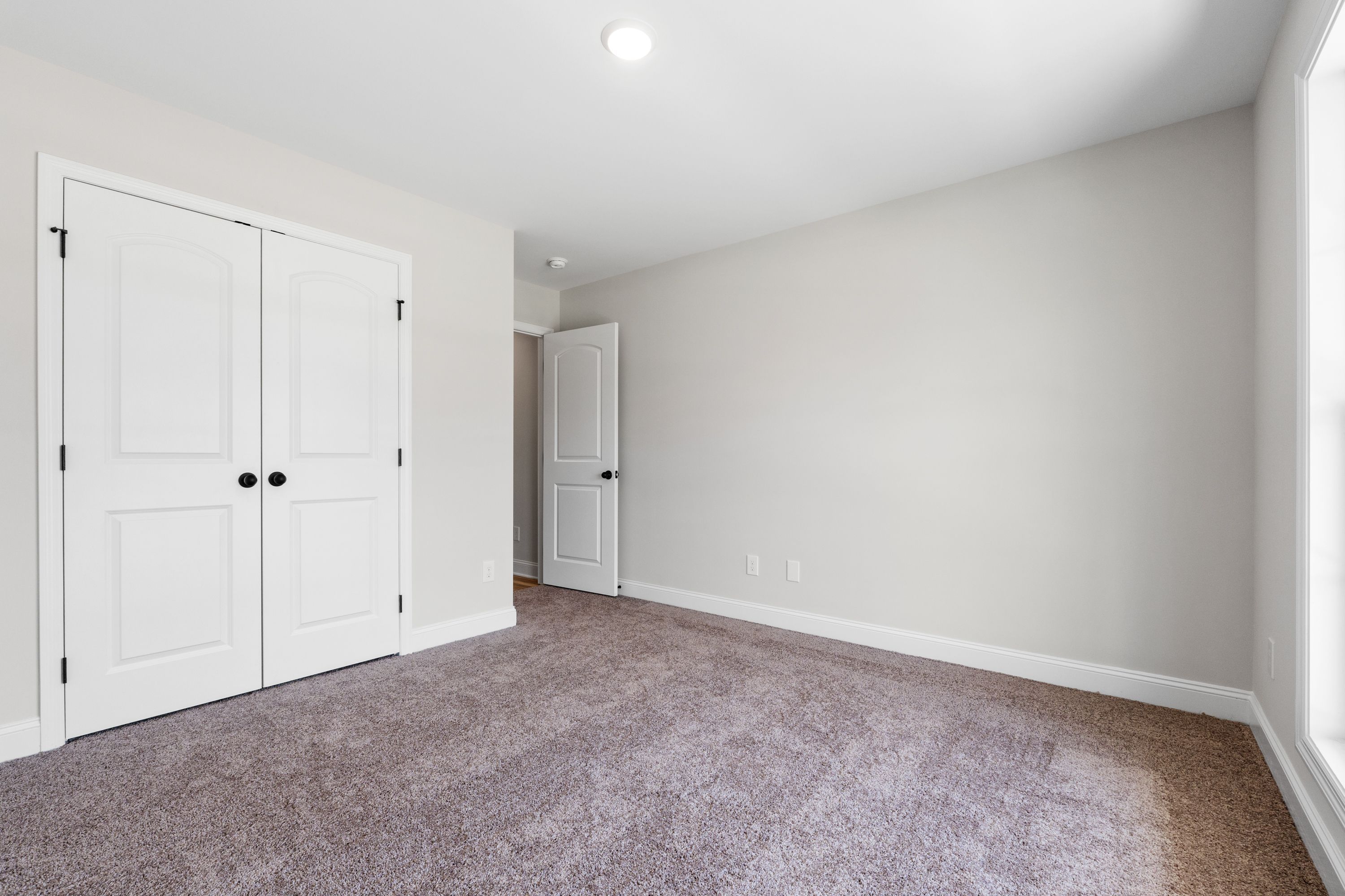 Spacious bedroom in The Holly C home design featuring plush carpeting, crisp white walls, and double-door closet.