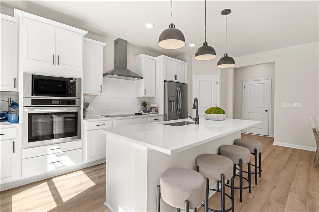 Modern white shaker kitchen with quartz island, stainless double oven, French door fridge, and upholstered bar stools in Davidson Homes The Burton B, Canton GA