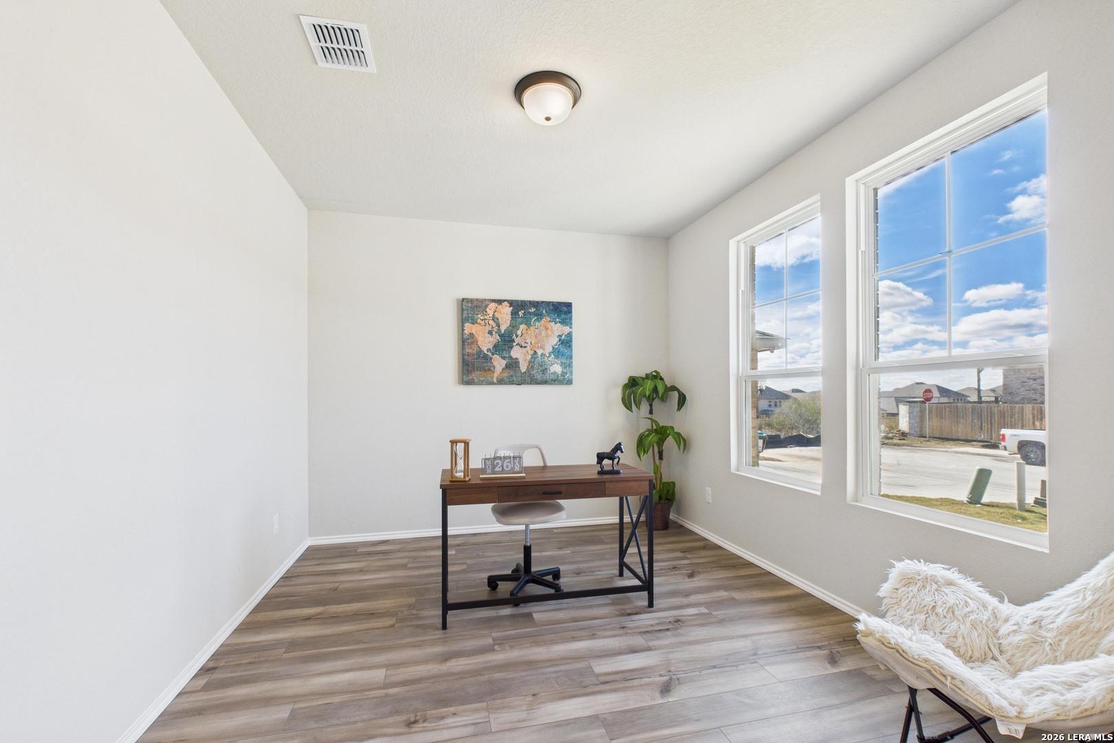 Bright home office with wooden desk, large sunny windows, potted plant, abstract art, and plush armchair in Davidson Homes The Douglas E, San Antonio