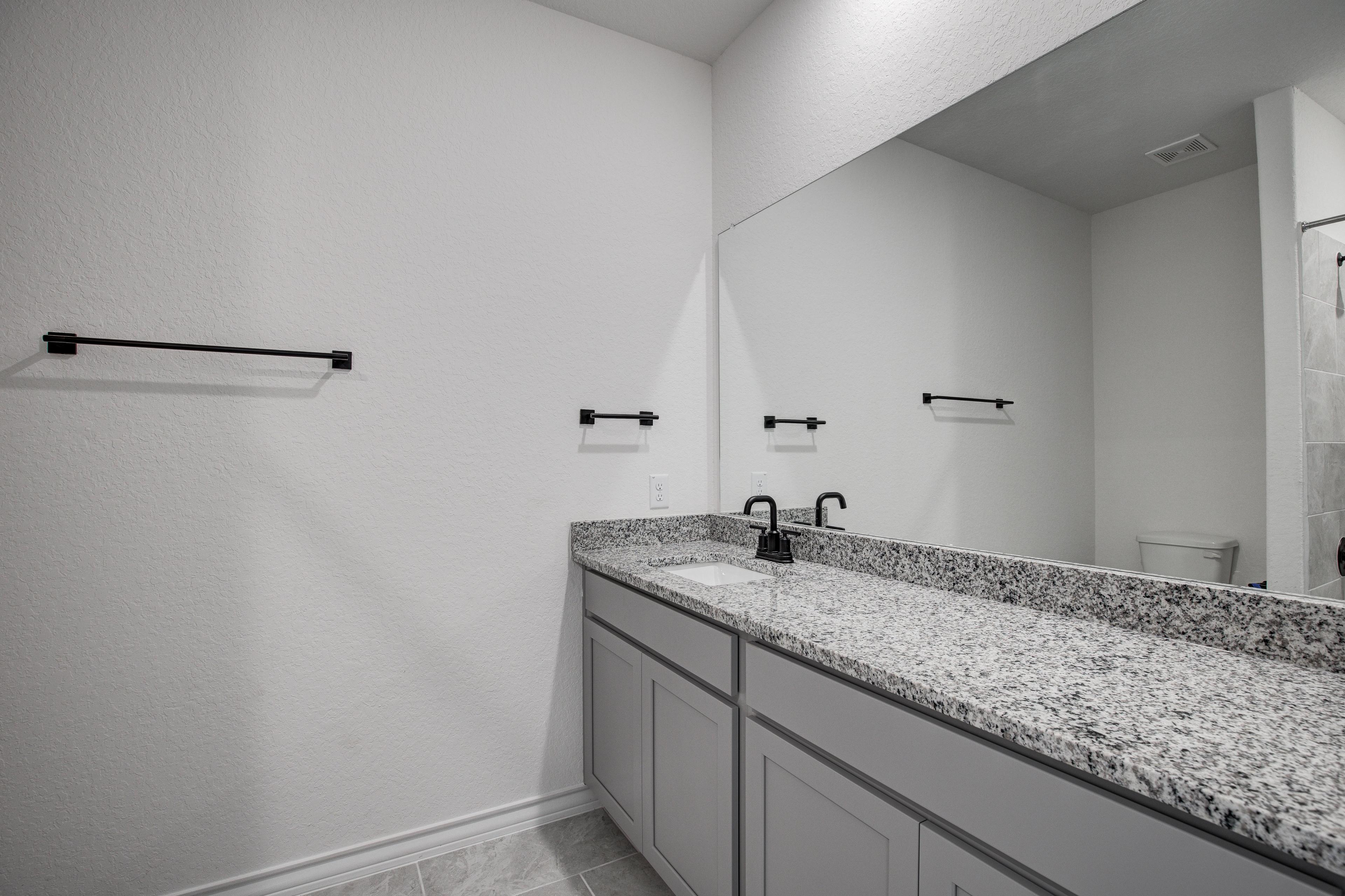 Modern master bathroom in The Lanier with double granite vanity, gray cabinets, large mirror, and black accents