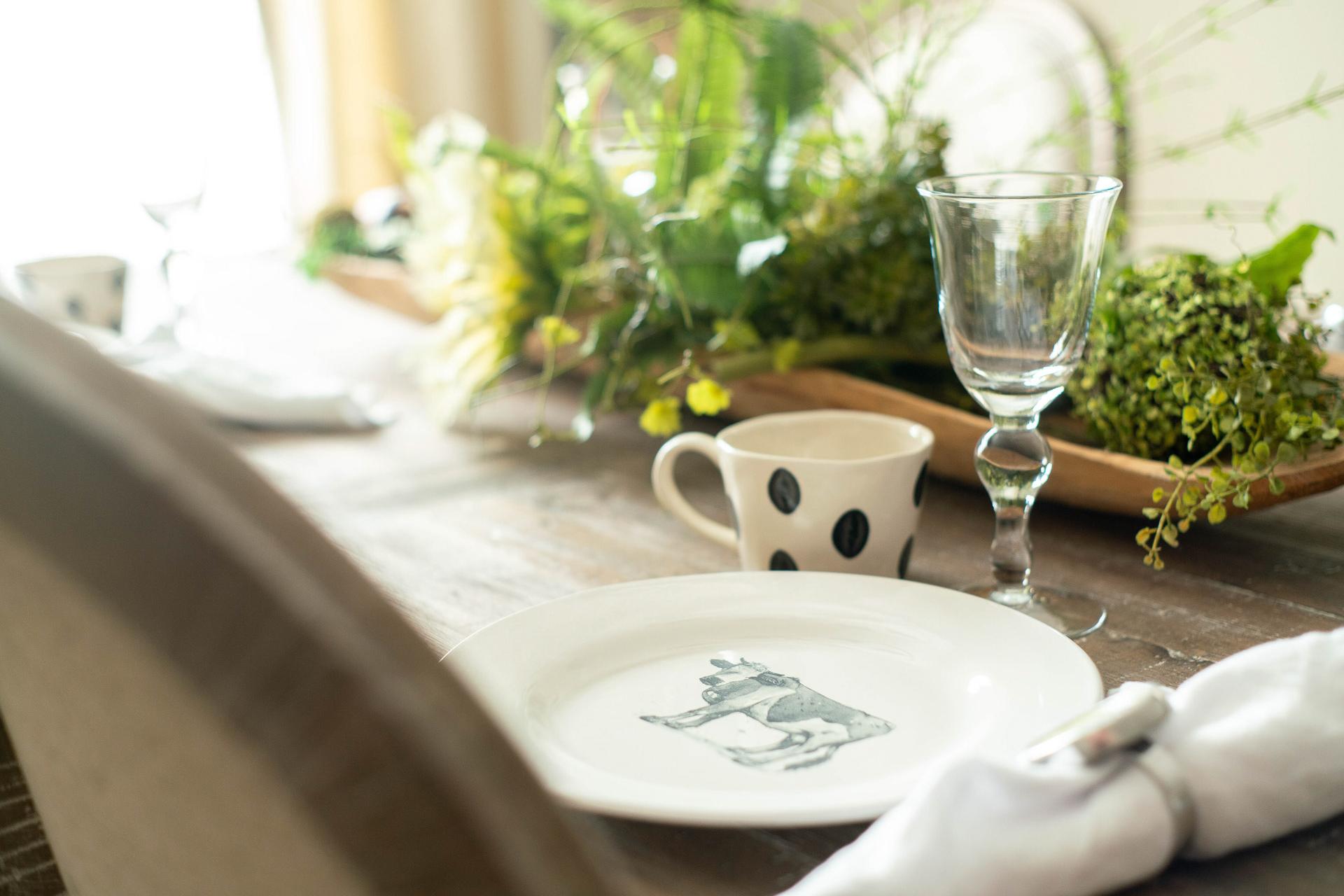 Elegant dining table at The Dairy at Oak Grove in South Huntsville, AL with cow-patterned plate, polka dot mug, wine glass, and fresh greenery
