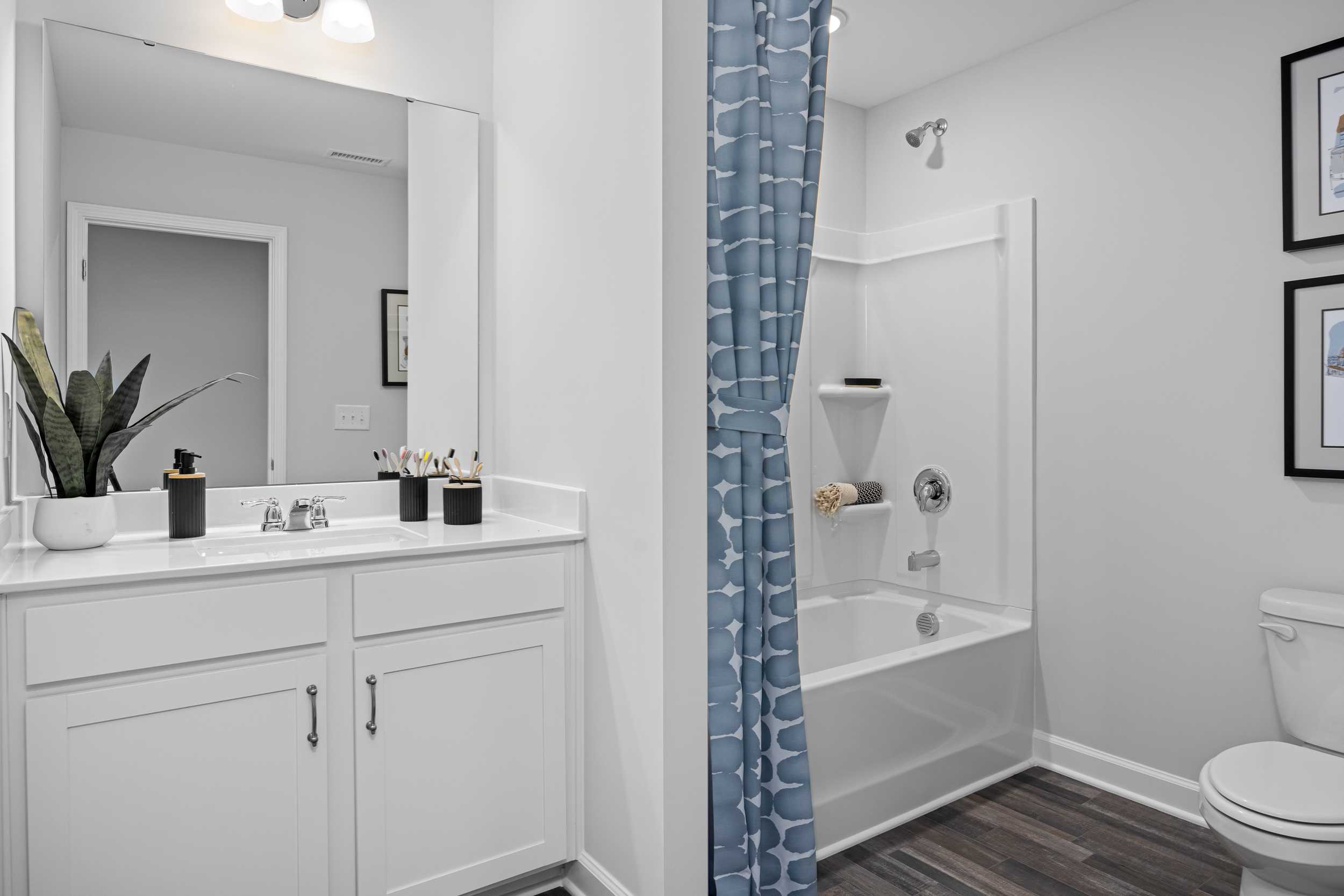 Modern master bathroom at Tobacco Road in Angier NC with white double vanity, blue-curtained shower, bathtub by Davidson Homes