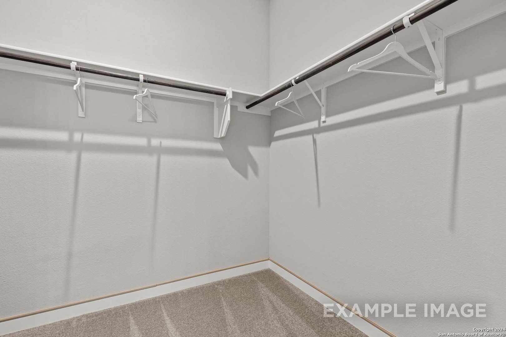 Spacious walk-in closet with white walls, hanging rods, and brackets in master suite of Davidson Homes The Collin A in Seguin, Texas