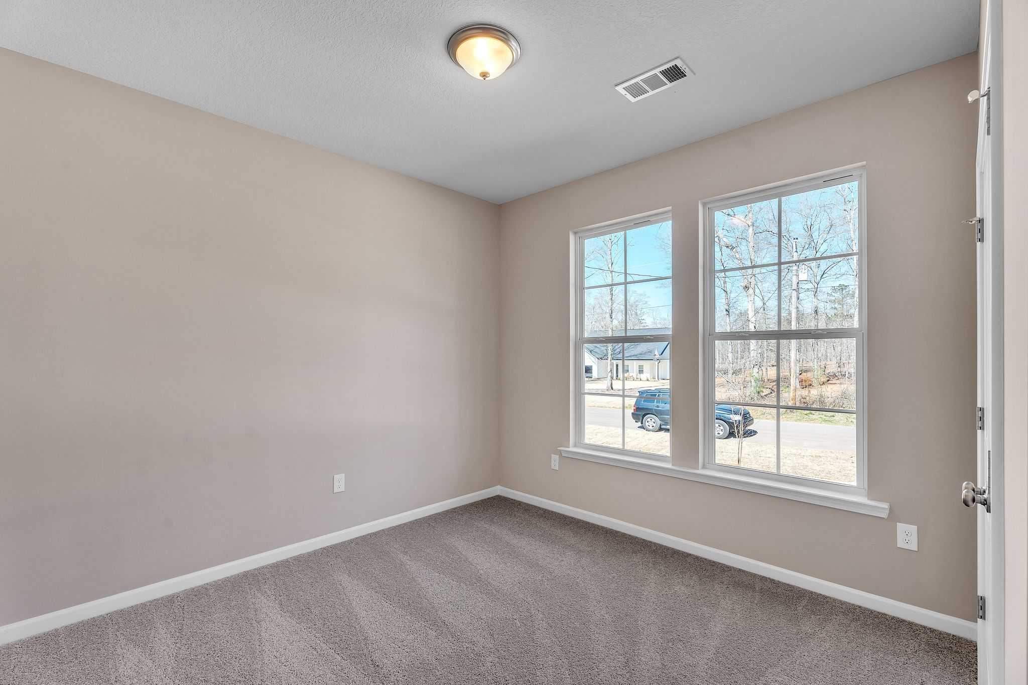 Spacious empty bedroom with beige walls, carpeted floor, and large windows in Anderson Lakes, Opelika AL by Davidson Homes