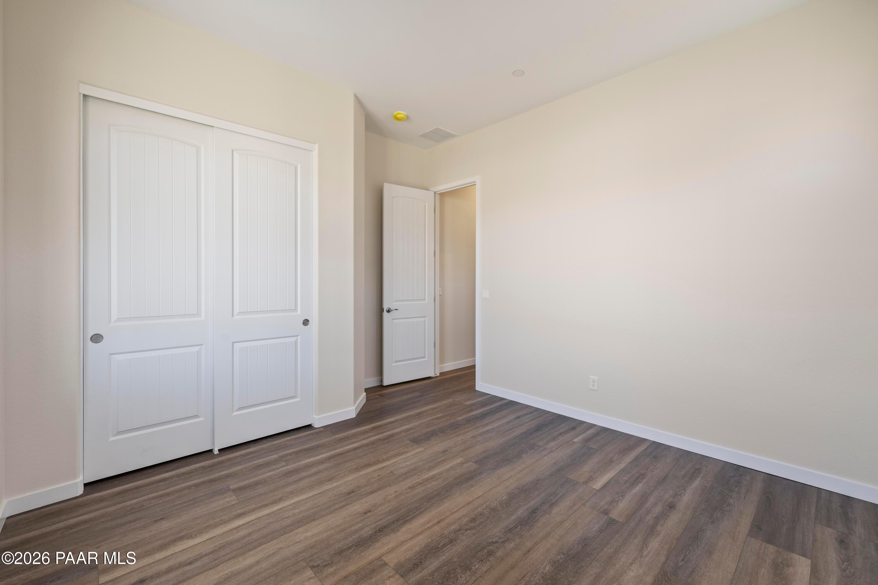 Bright secondary bedroom with white double closet doors, bath entry, and luxury vinyl plank flooring in Davidson Homes The Soleil E, Prescott, Arizona