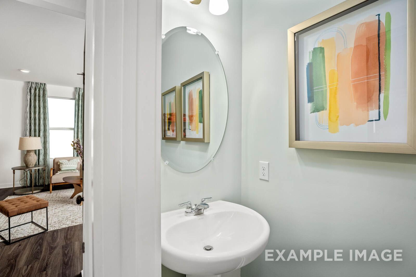 Modern master bathroom in The Gordon C showcasing round mirror, abstract wall art, and open door to wood-floored bedroom
