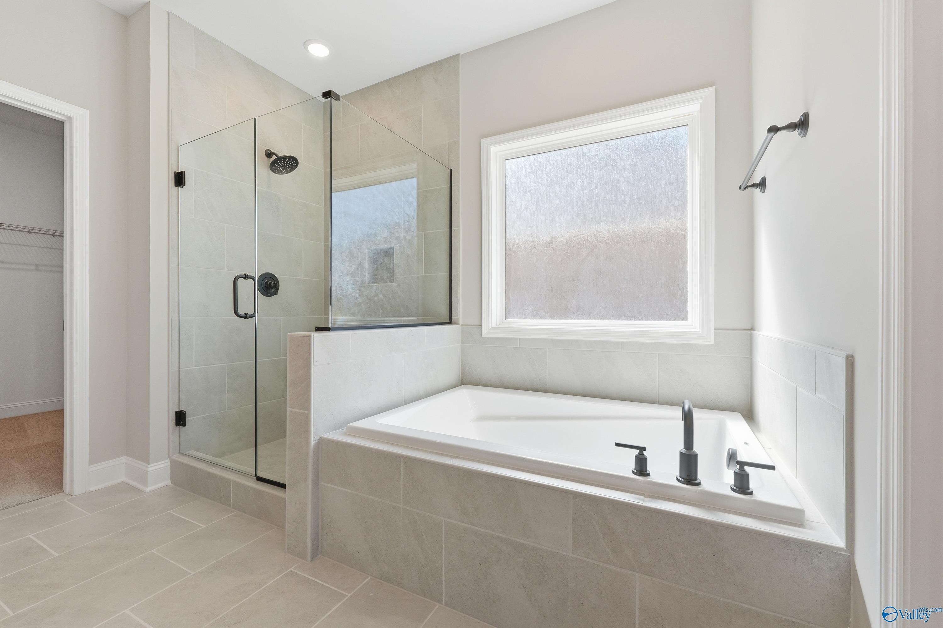 Modern master bathroom featuring frameless glass shower, soaking tub, and tiled floors in Davidson Homes The Rockford, Harvest, Alabama