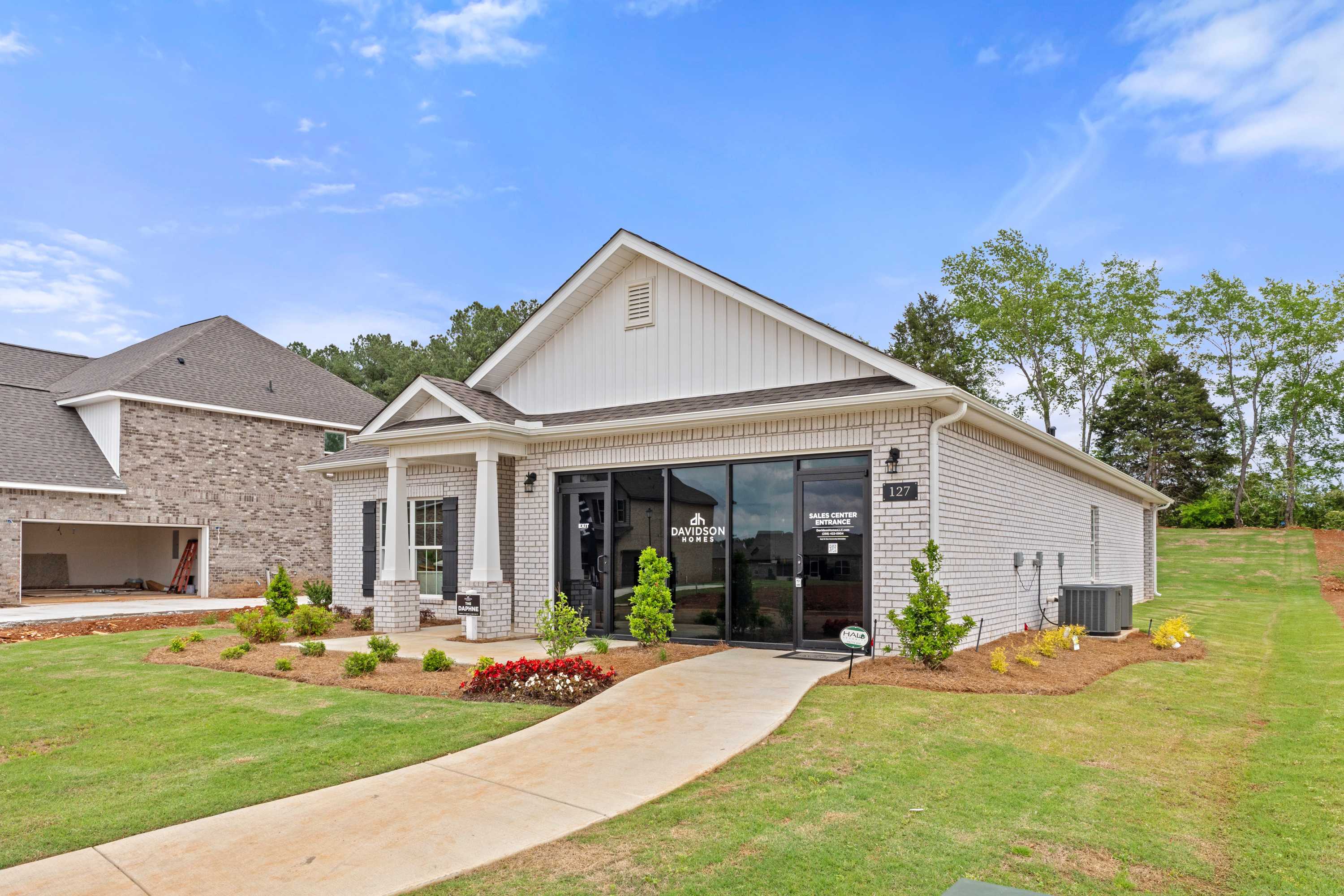 White brick model home at Ivy Hills in Toney, Alabama by Davidson Homes with black glass entrance, columns, and landscaped walkway