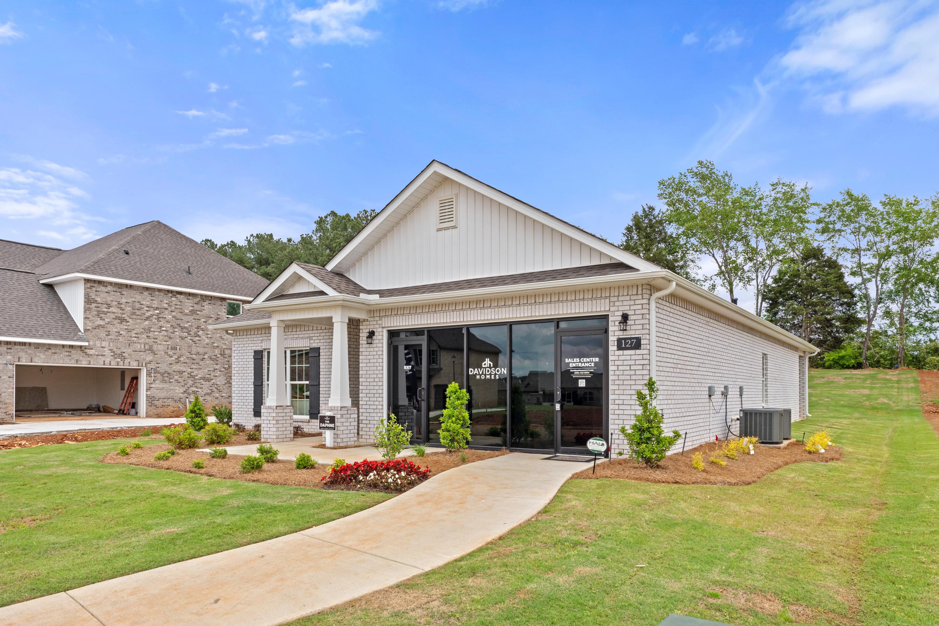 White brick model home at Ivy Hills in Toney, Alabama by Davidson Homes with black glass entrance, columns, and landscaped walkway