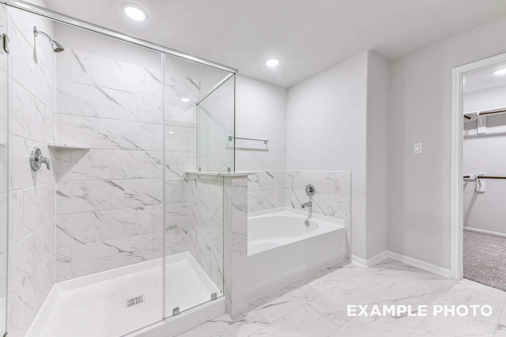 Spacious master bathroom in The Laguna A home: frameless glass shower, freestanding soaking tub, white marble tiles