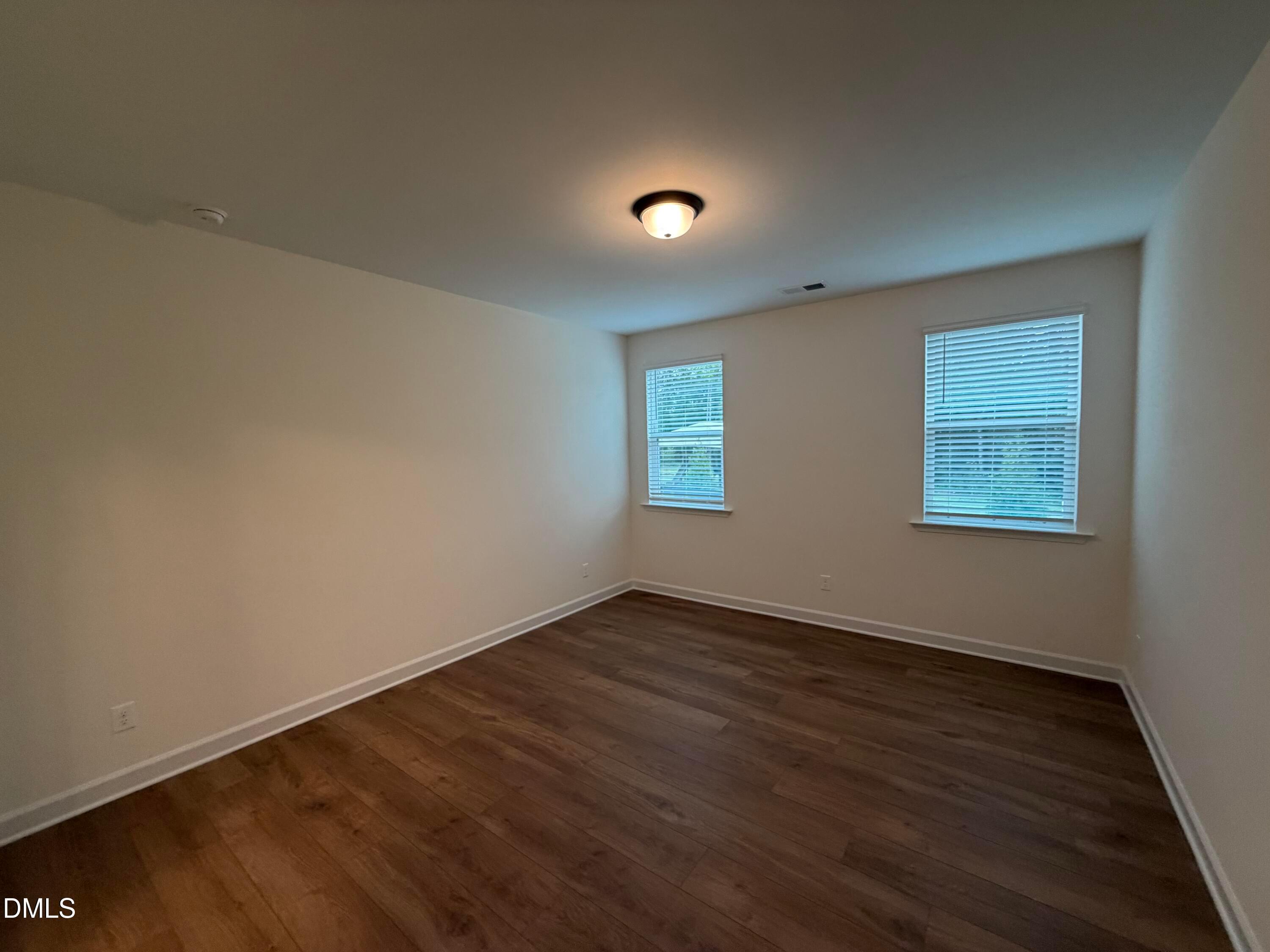 Bright empty bedroom with wood-look flooring and two windows in Davidson Homes The Ashport M, Wendell Ridge, North Carolina