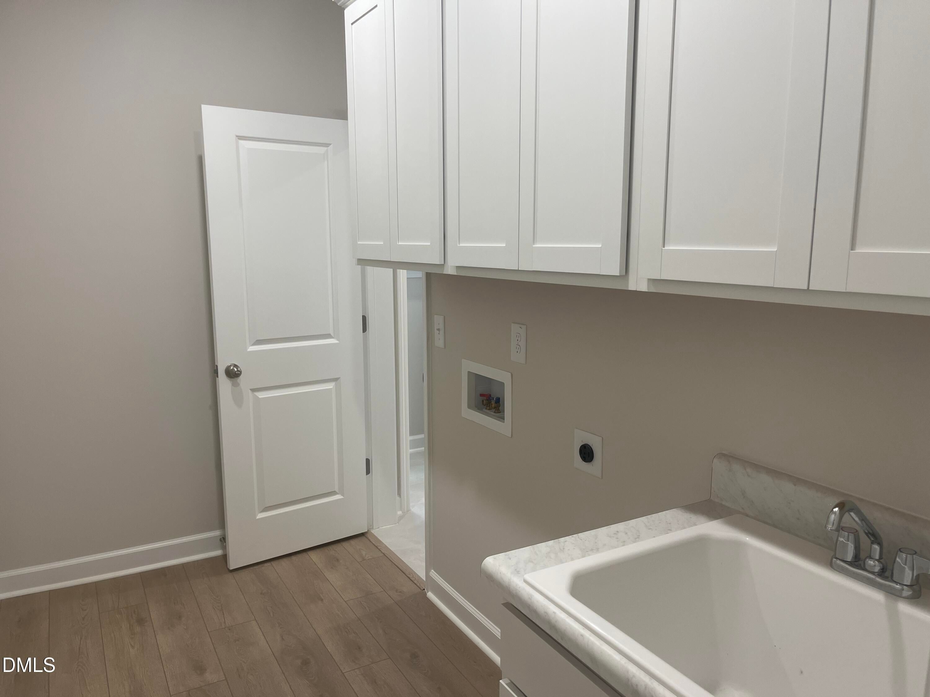 Modern laundry room featuring white shaker cabinets, deep utility sink, and hardwood floors in Davidson Homes The Ashport G, Wake Forest NC