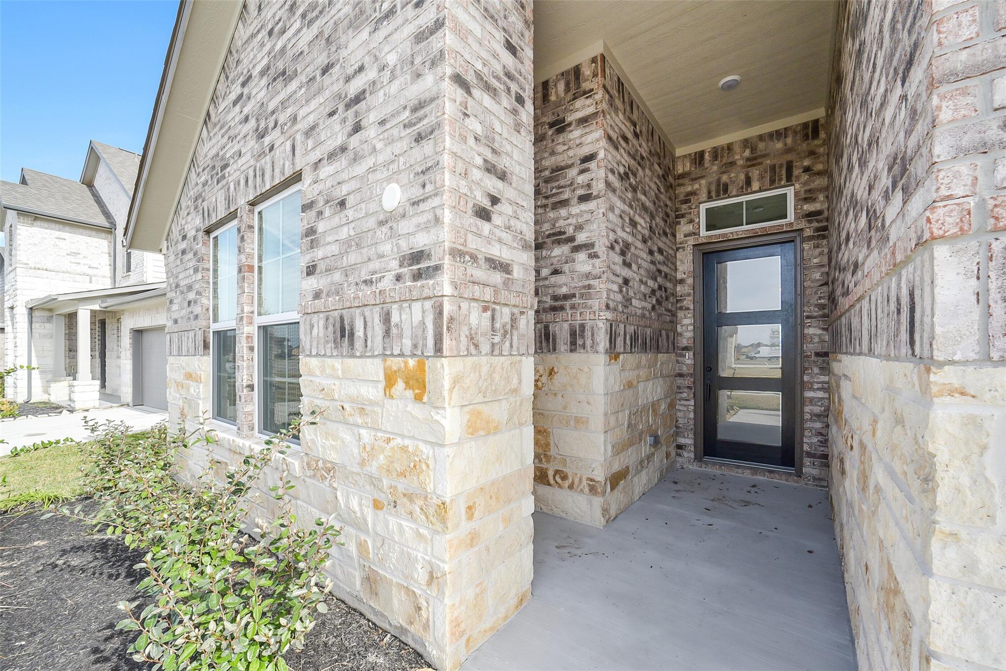 Modern brick exterior with glass front door, covered entry porch, and landscaped curb appeal in 4-bedroom Davidson Homes George B, Rosharon, TX