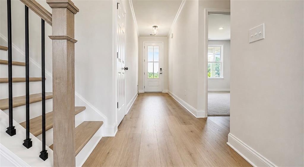 Bright entryway with hardwood floors and wooden staircase in The Hickory C floor plan by Davidson Homes in Hoschton, GA.