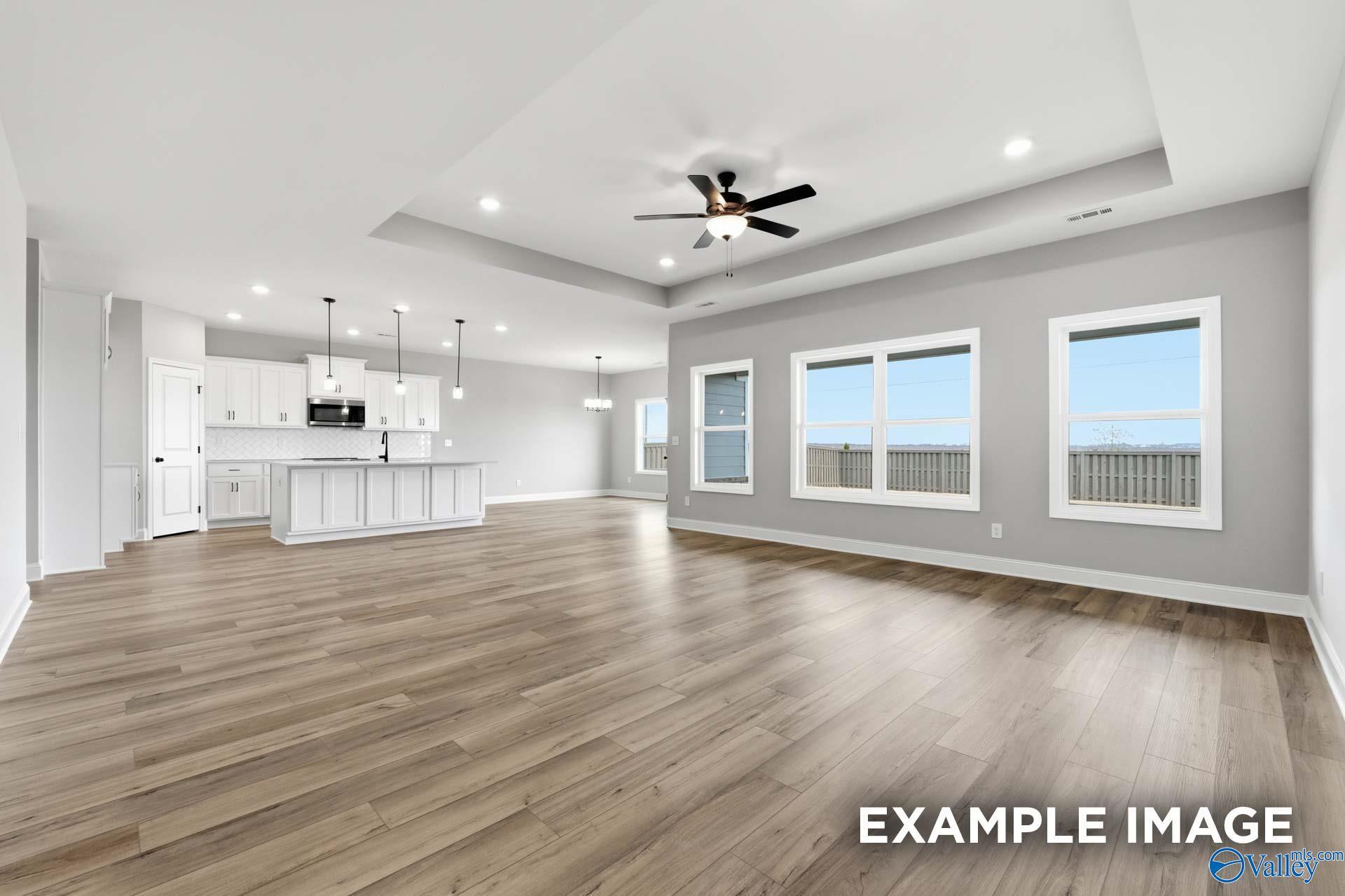 Open-concept great room with luxury vinyl plank flooring, tray ceiling, and white kitchen in Davidson Homes Rockford C, Athens, AL