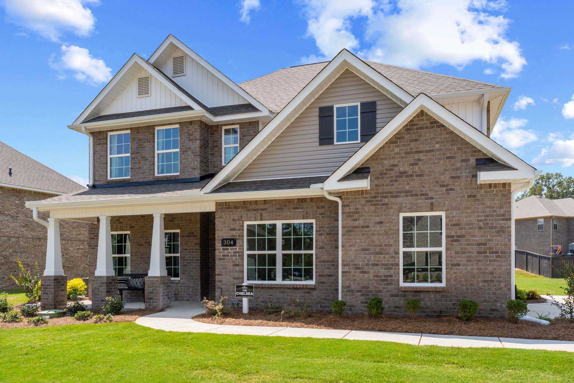 Two-story brick home exterior at Creek Grove in New Market, Alabama with covered front porch, white columns, and landscaped yard