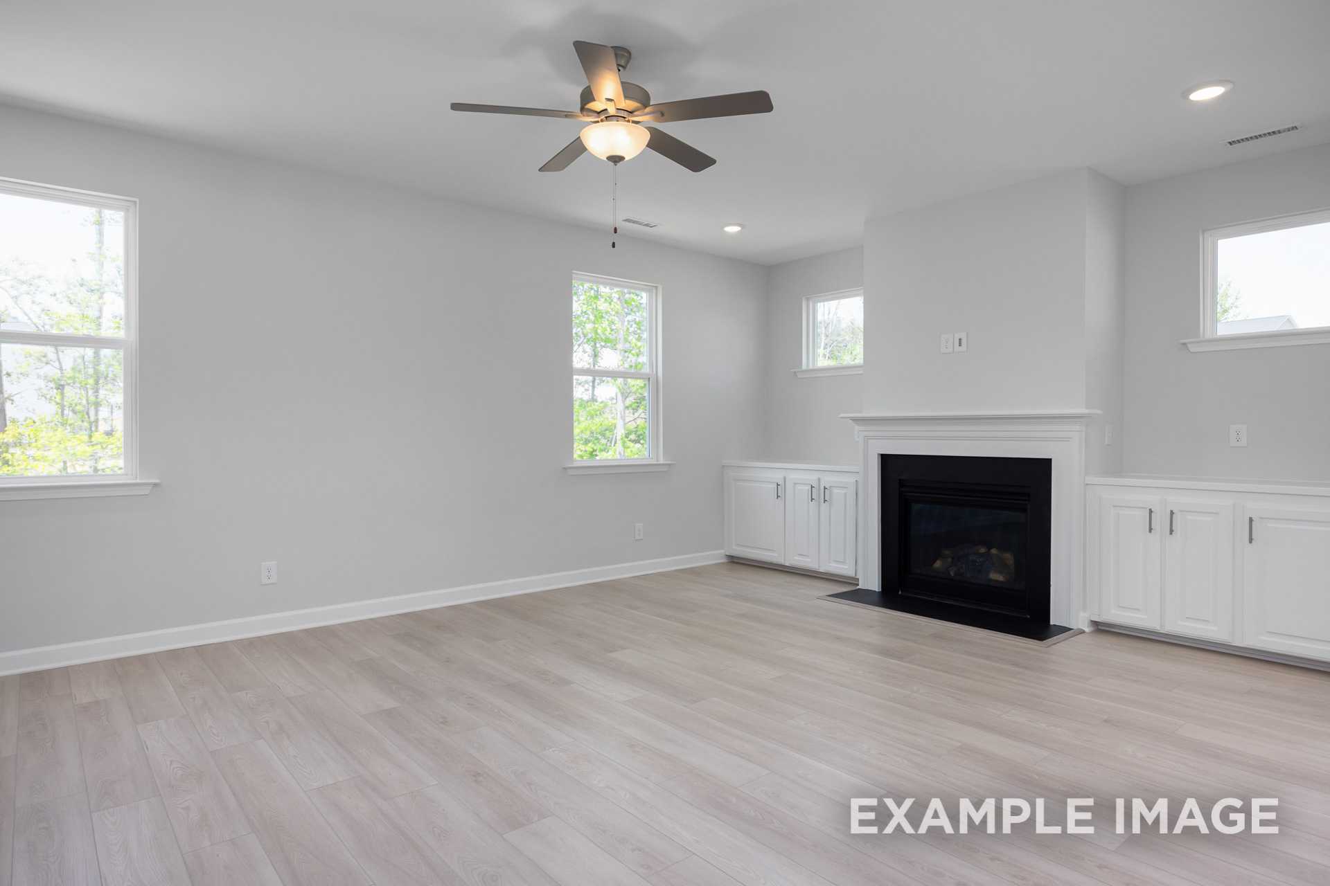 Spacious living room in The Gavin C by Davidson Homes with gas fireplace, white cabinets, ceiling fan, and large windows