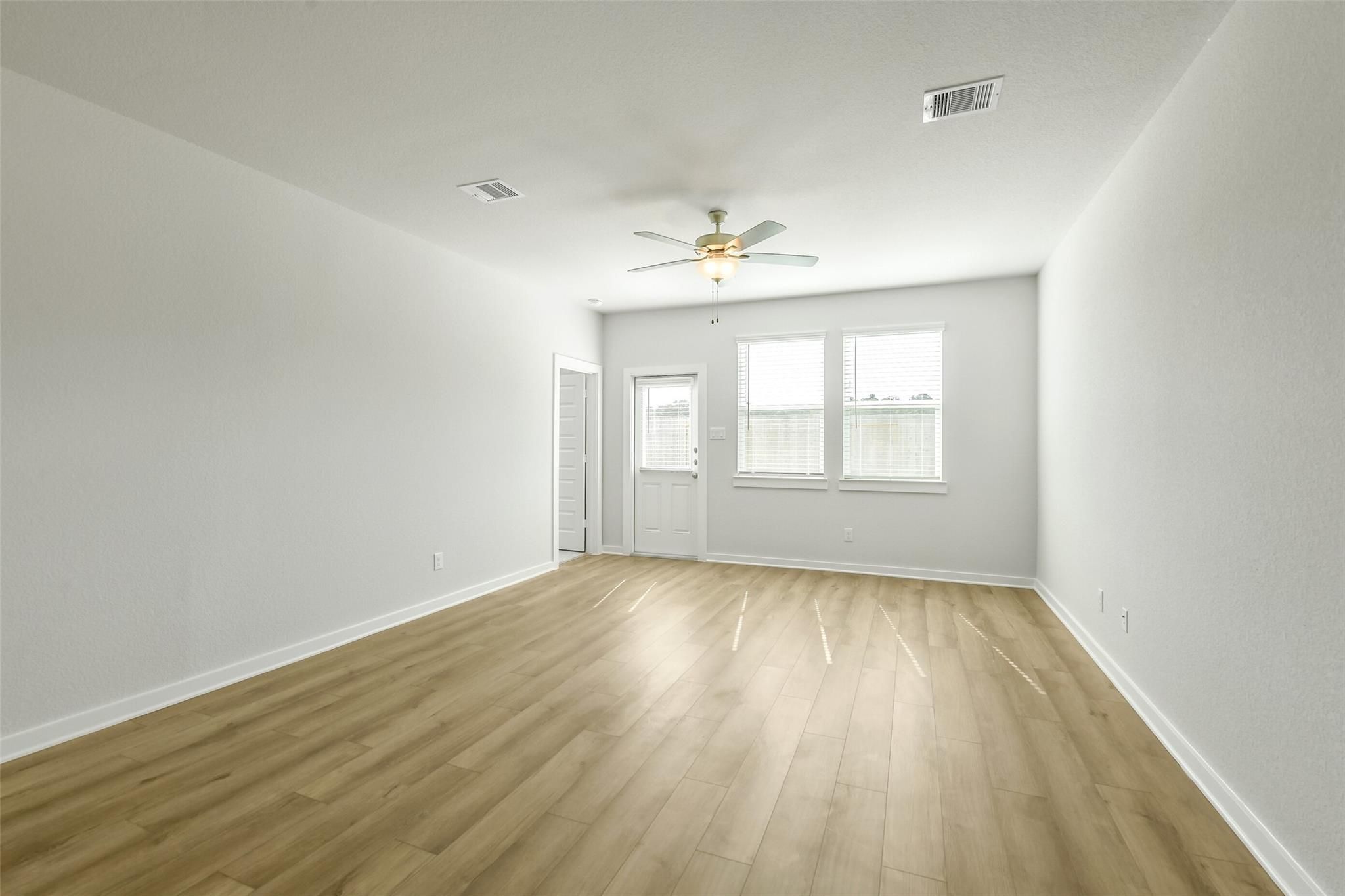 Bright empty living room with light wood floors, ceiling fan, and large windows in Davidson Homes The San Marcos E, Cleveland, Texas