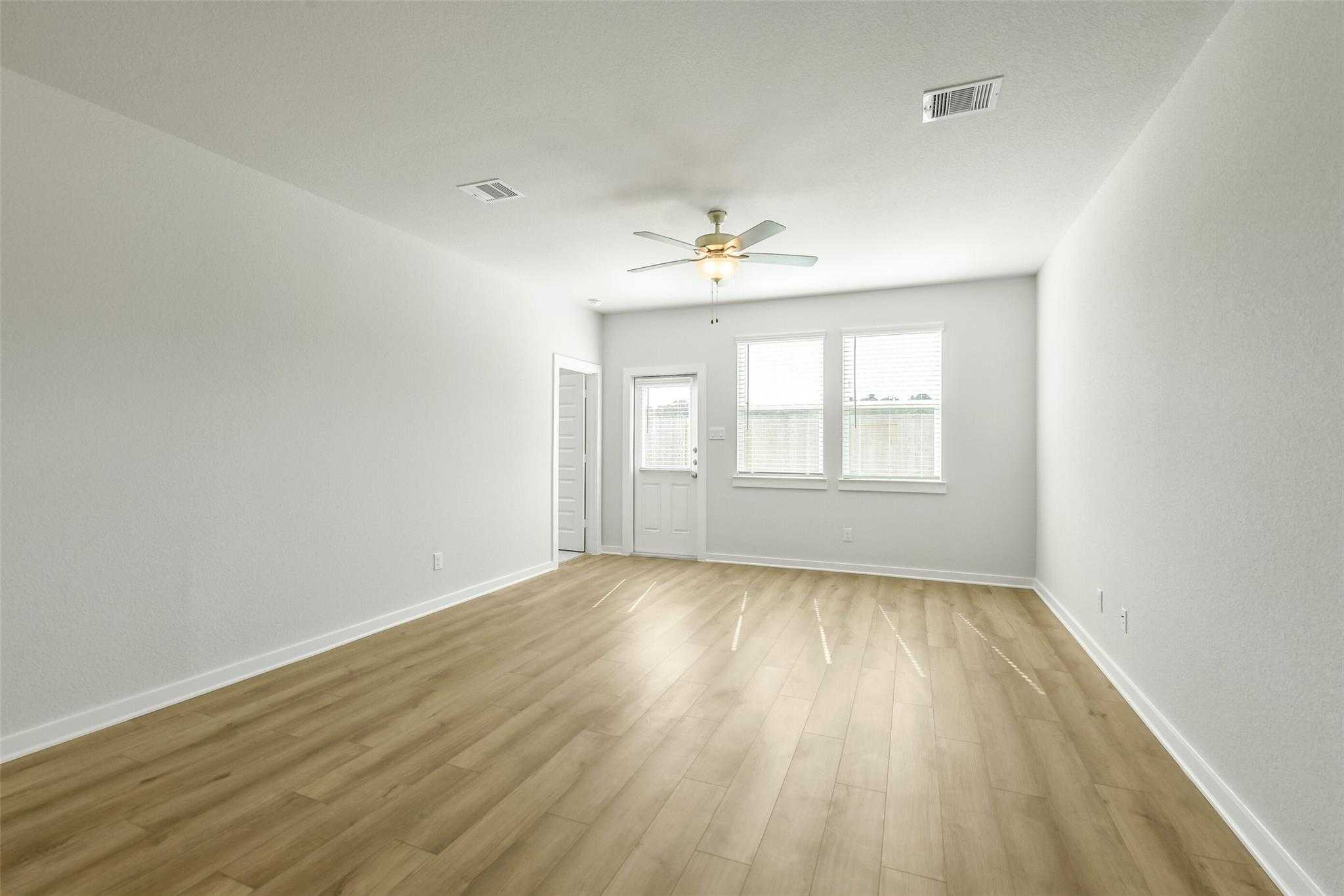 Bright empty living room with light wood floors, ceiling fan, and large windows in Davidson Homes The San Marcos E, Cleveland, Texas