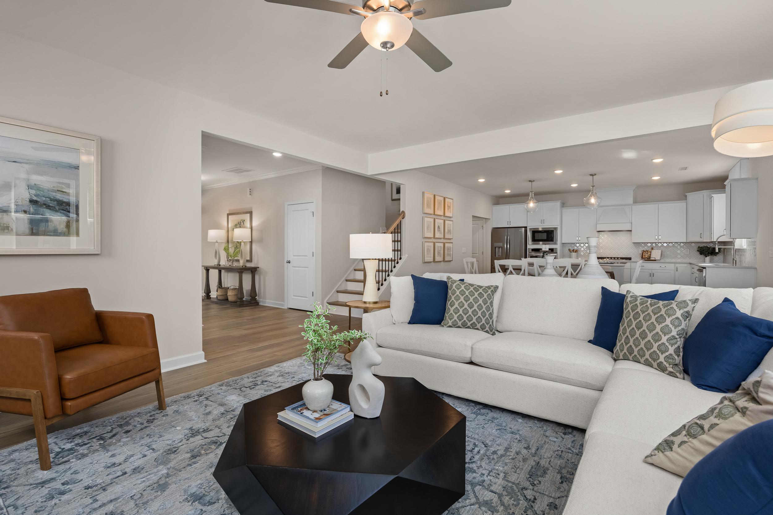 Open-concept living room in The Hickory II by Davidson Homes featuring white sectional sofa, leather armchair, modern coffee table, and kitchen view