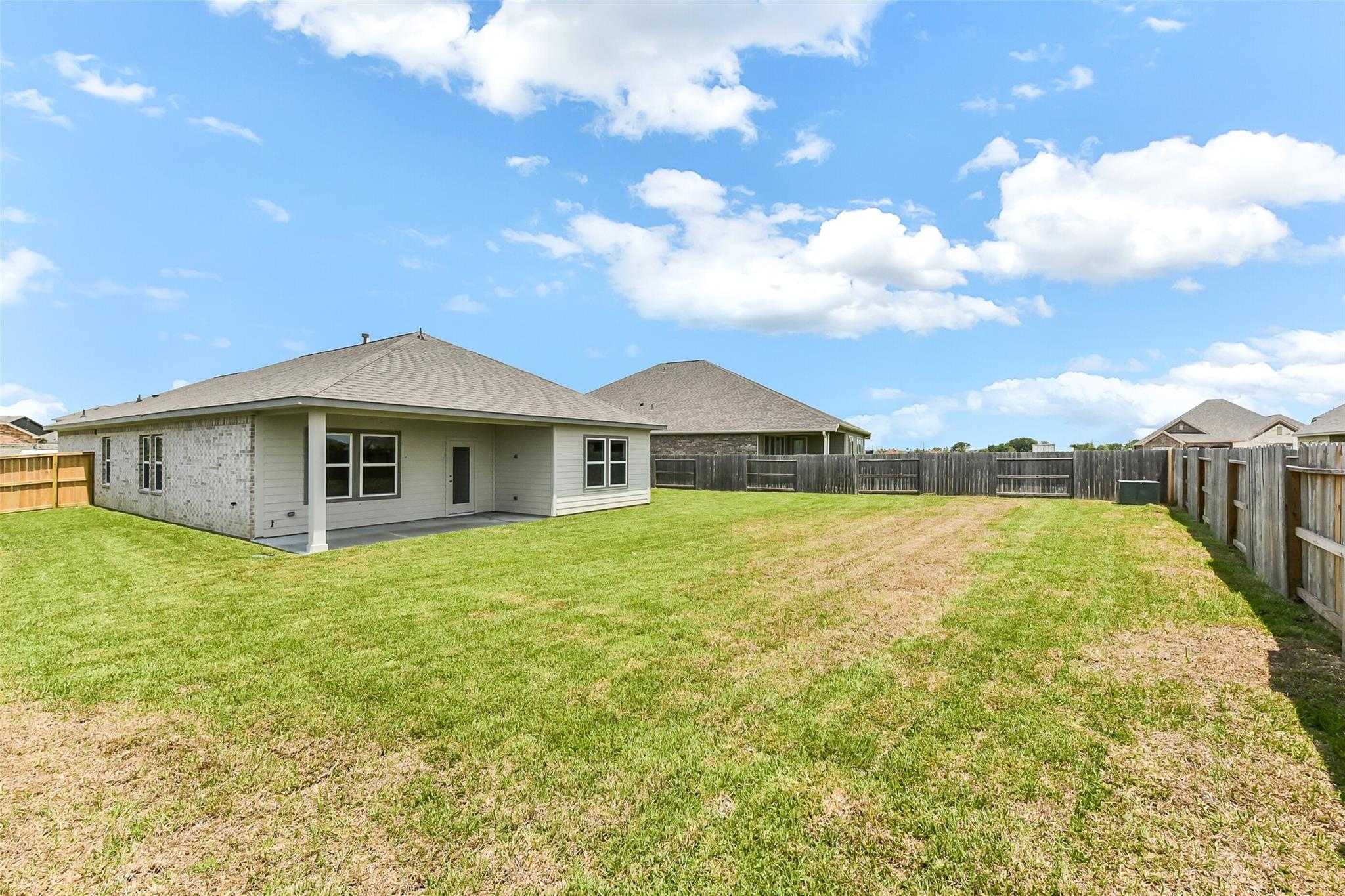 Beige single-story home with gabled roof, fenced grassy backyard, and neighboring houses in Sierra Vista, Rosharon, Texas