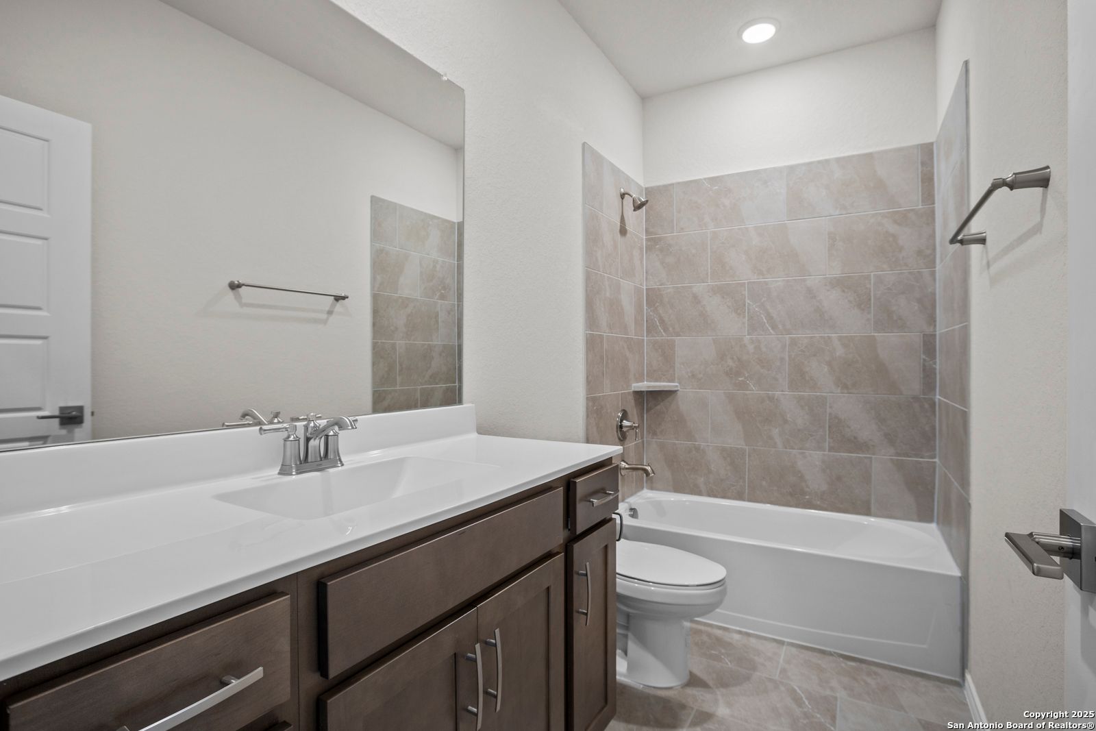 Spacious secondary bathroom with bathtub-shower combo, brown vanity, and beige tile in Davidson Homes The Asheville J, San Antonio