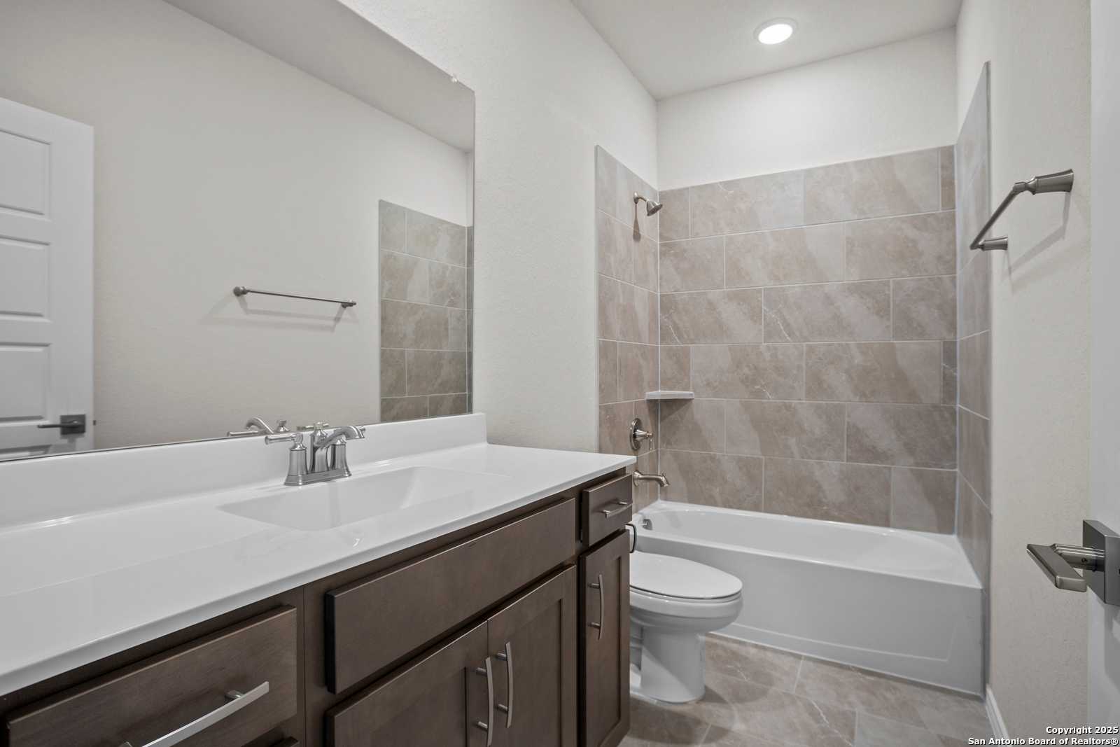 Spacious secondary bathroom with bathtub-shower combo, brown vanity, and beige tile in Davidson Homes The Asheville J, San Antonio